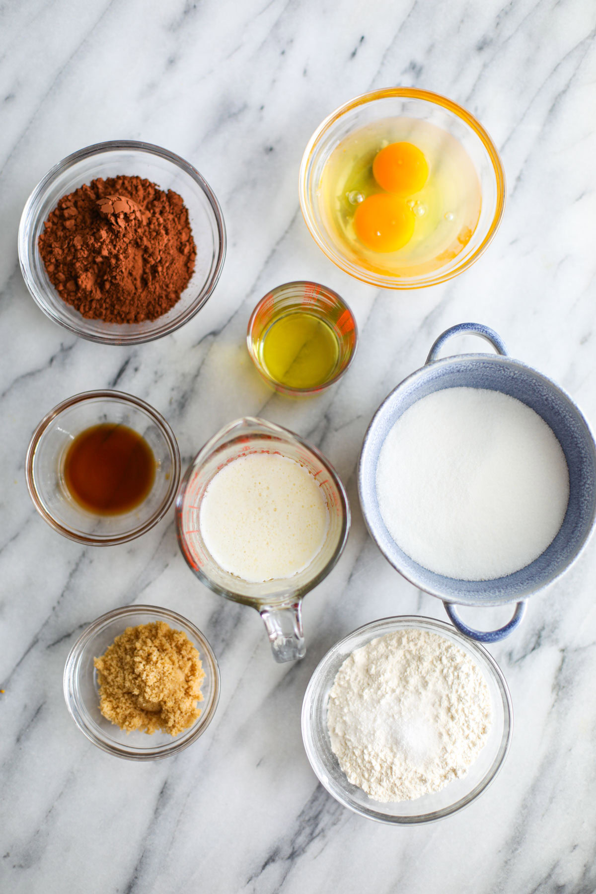 Bowls of brownie batter ingredients on a white marble table.