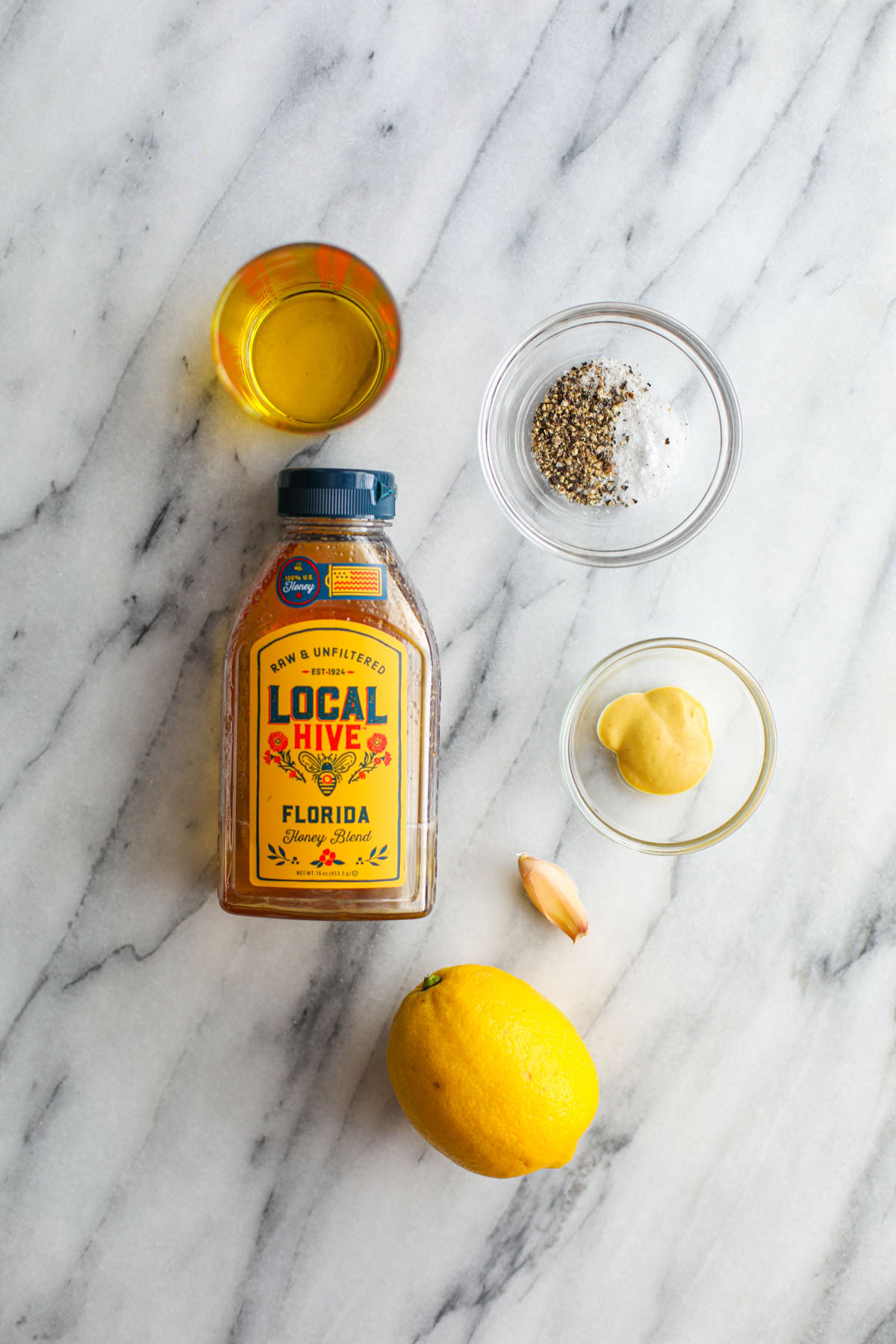 A bottle of honey, jar of olive oil, seasonings, and a garlic clove.