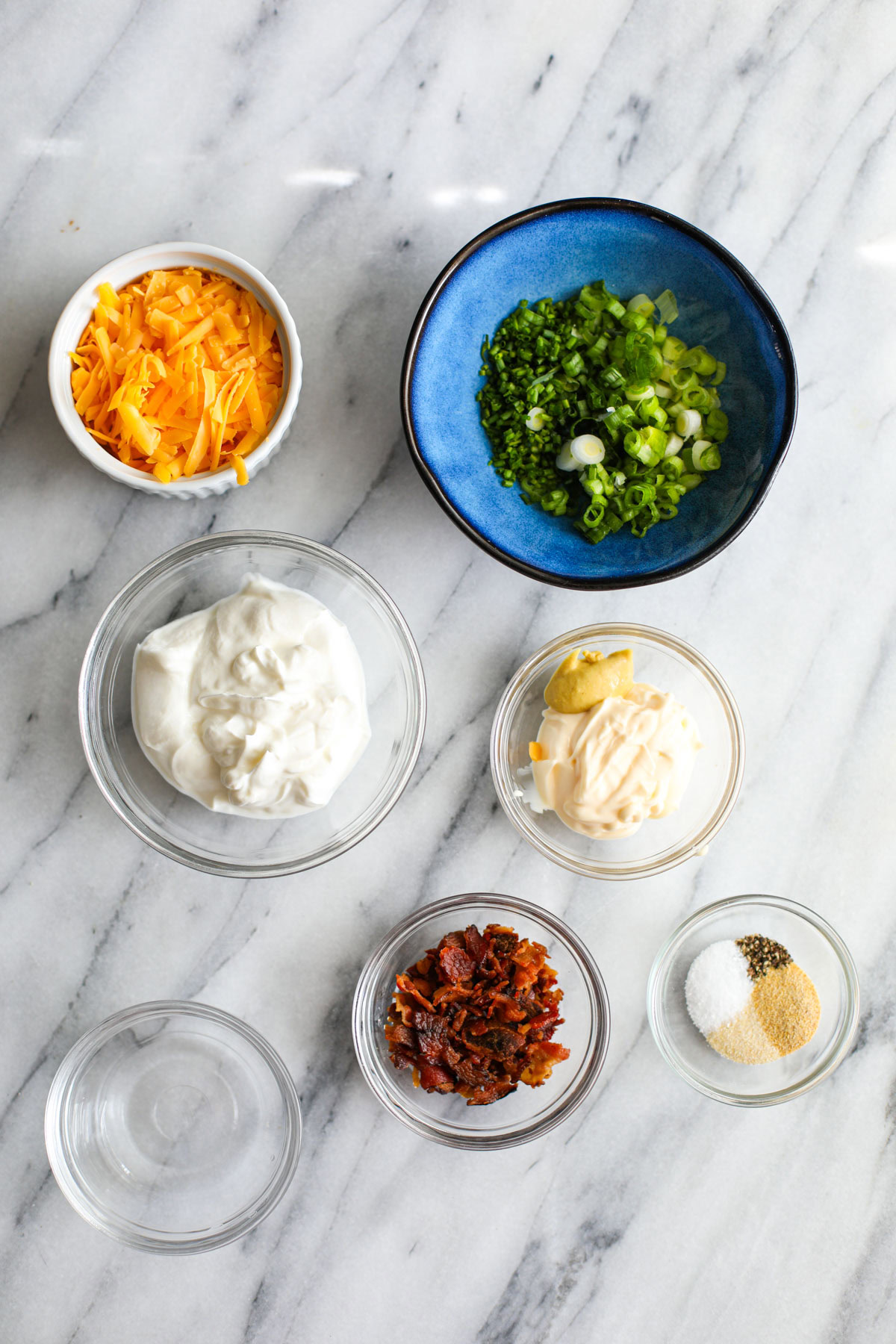 Bowls of cheese, green onions, sour cream, mayonnaise, vinegar, bacon, and seasonings.