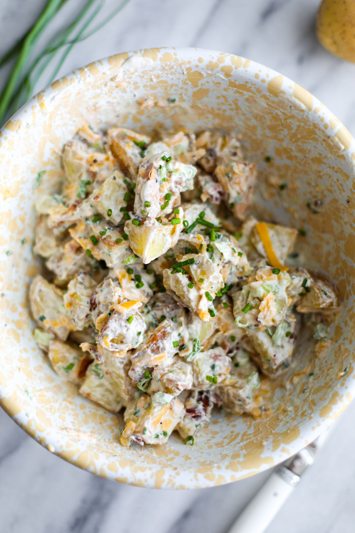Baked potato salad in a white and yellow bowl.