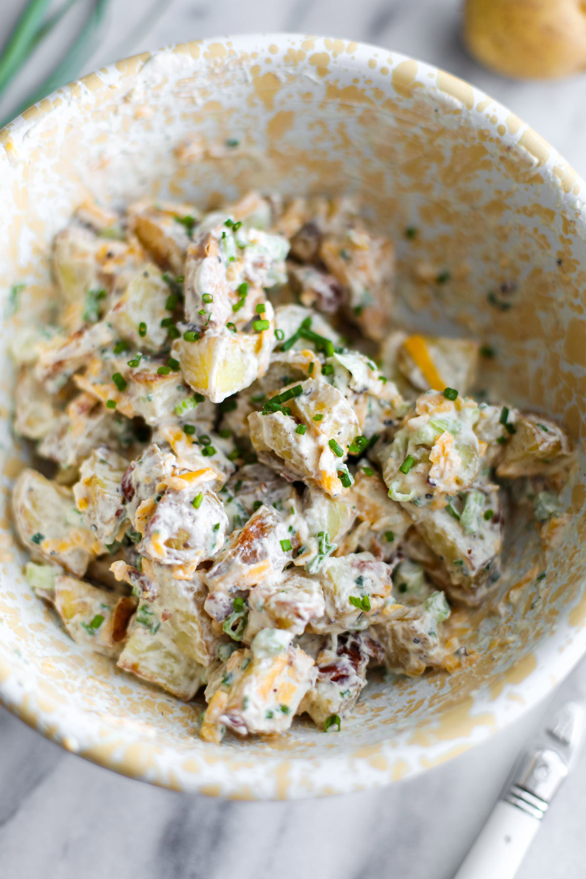 Baked potato salad in a white and yellow bowl.