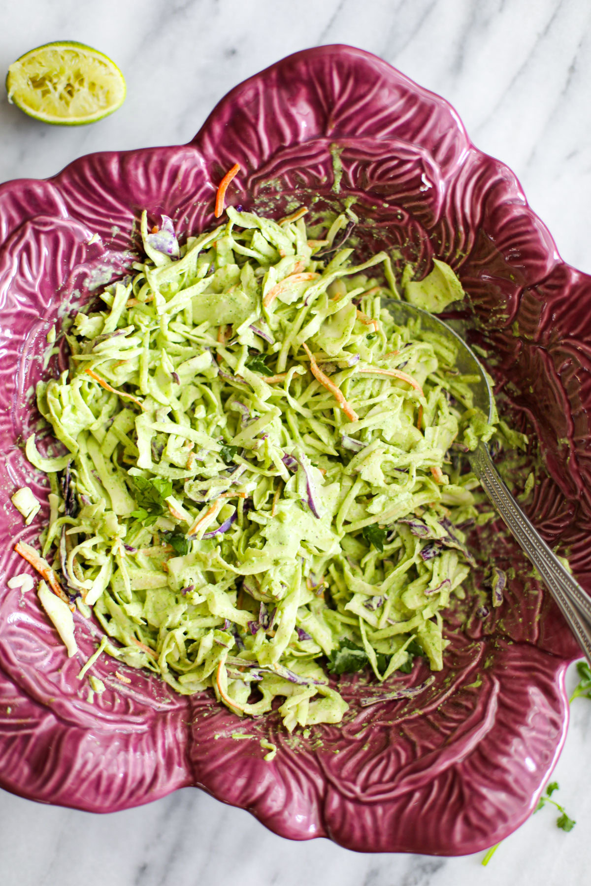 Cilantro lime coleslaw in a purple cabbage shaped bowl with a silver serving spoon.