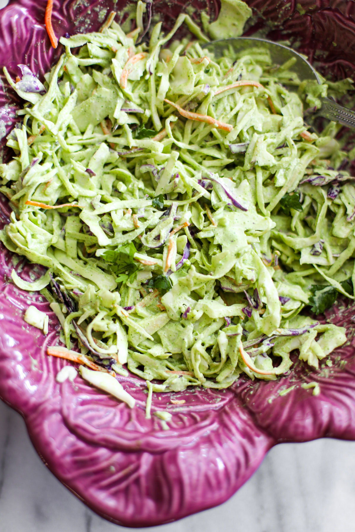 Cilantro lime coleslaw in a purple cabbage shaped bowl with a silver serving spoon.