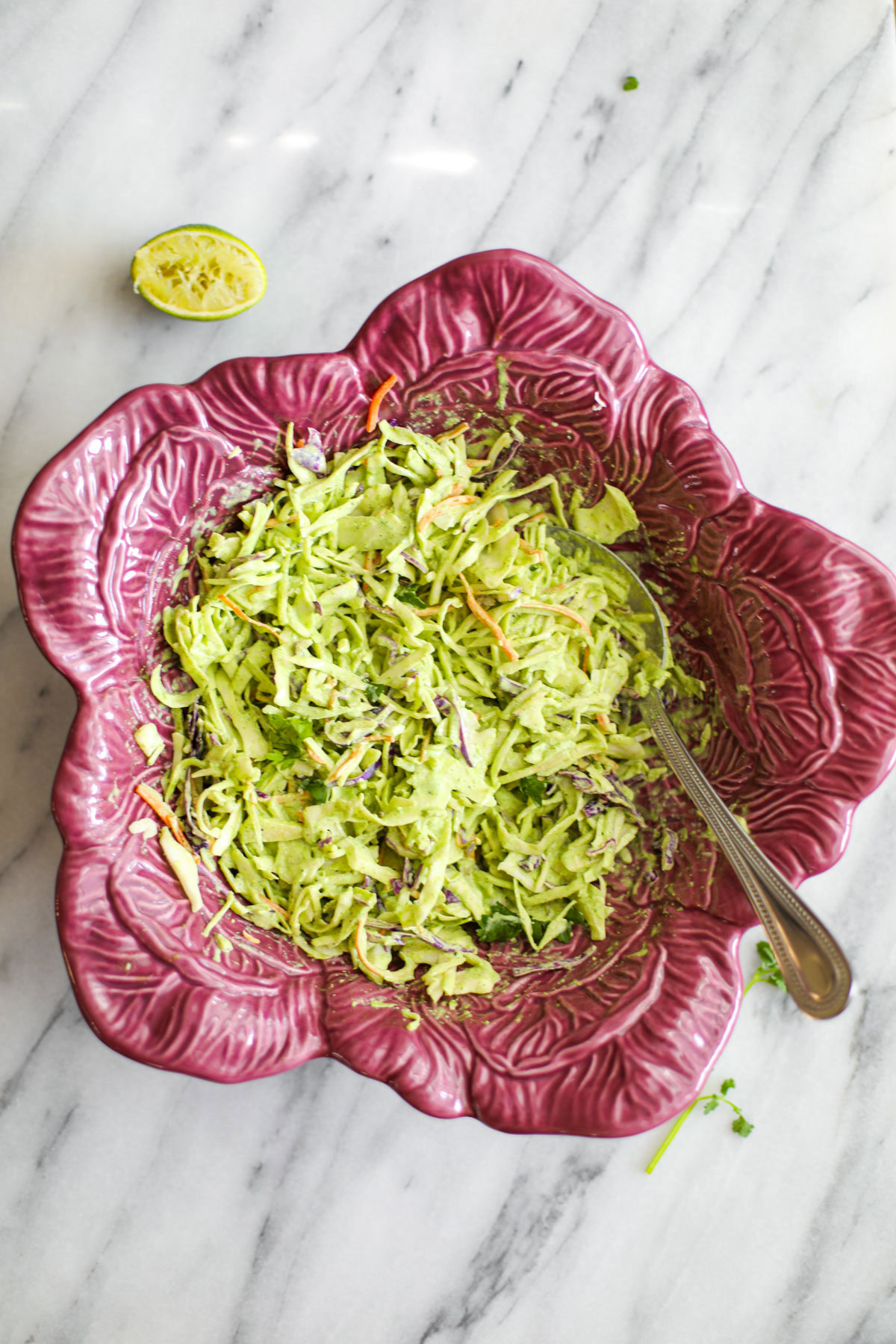 Cilantro lime coleslaw in a purple cabbage shaped bowl with a silver serving spoon.