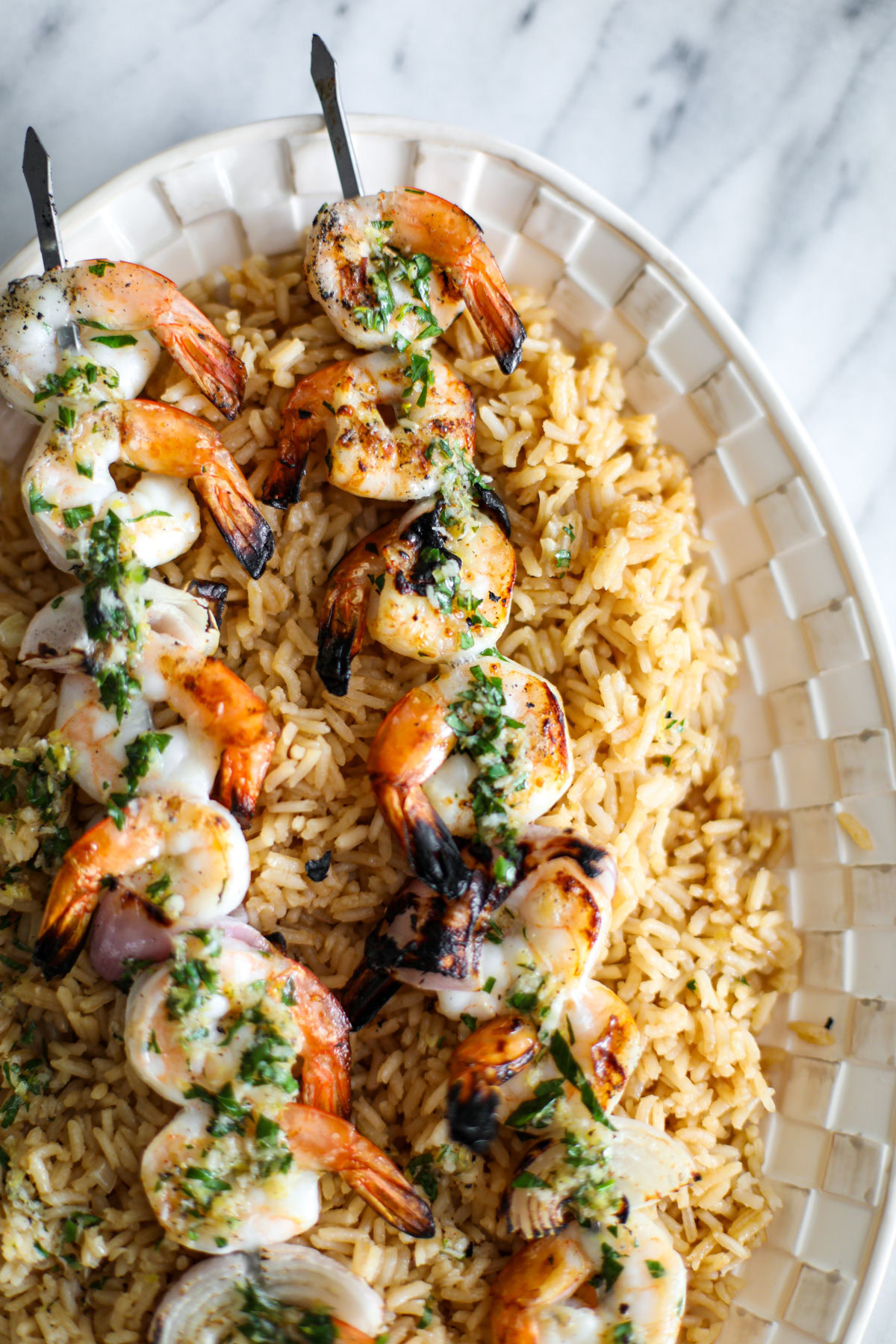 Grilled lemon herb shrimp on a bed of rice with a drizzle of herb sauce on a white platter.