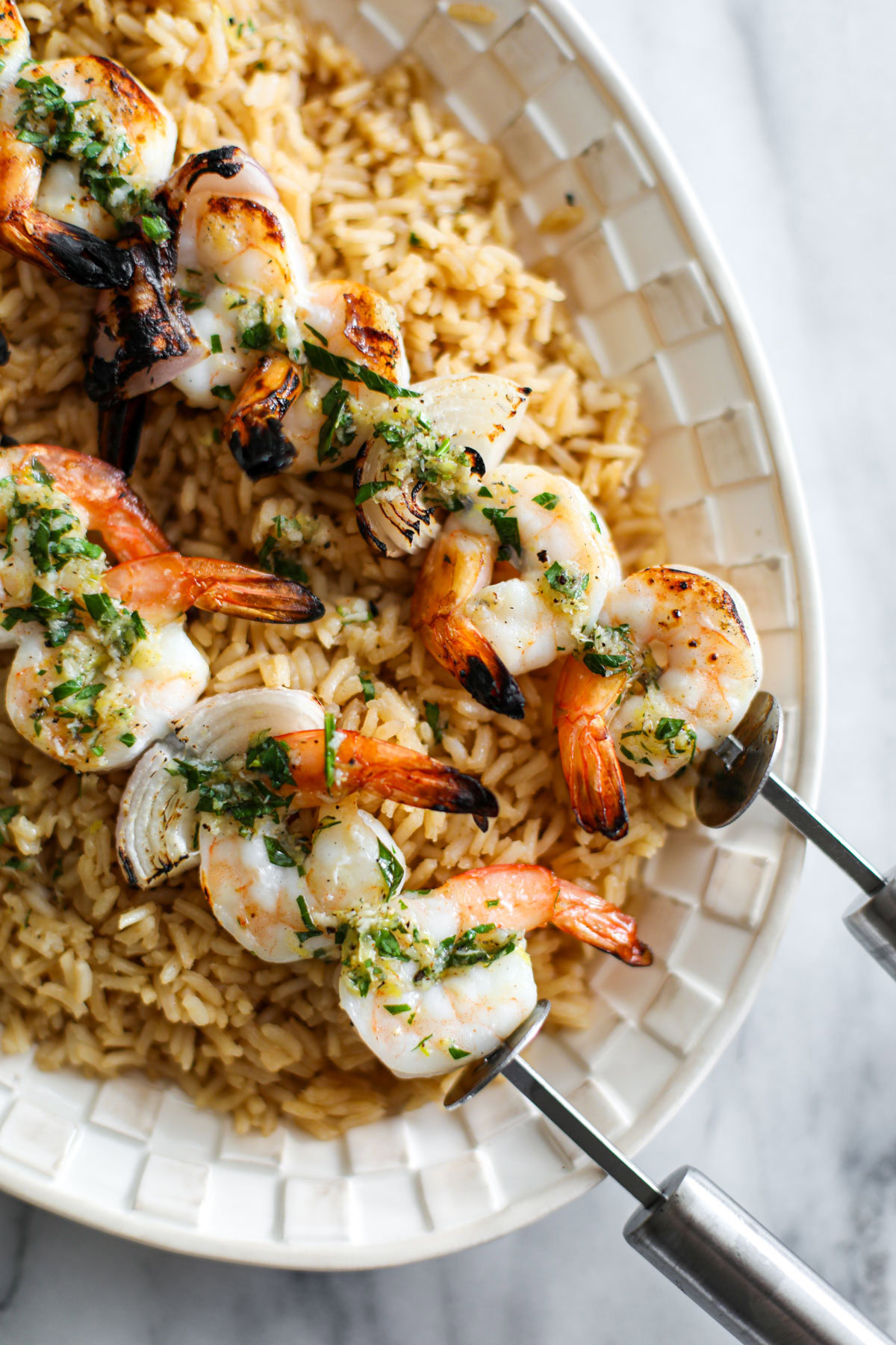 Grilled lemon herb shrimp on a bed of rice on a white platter.