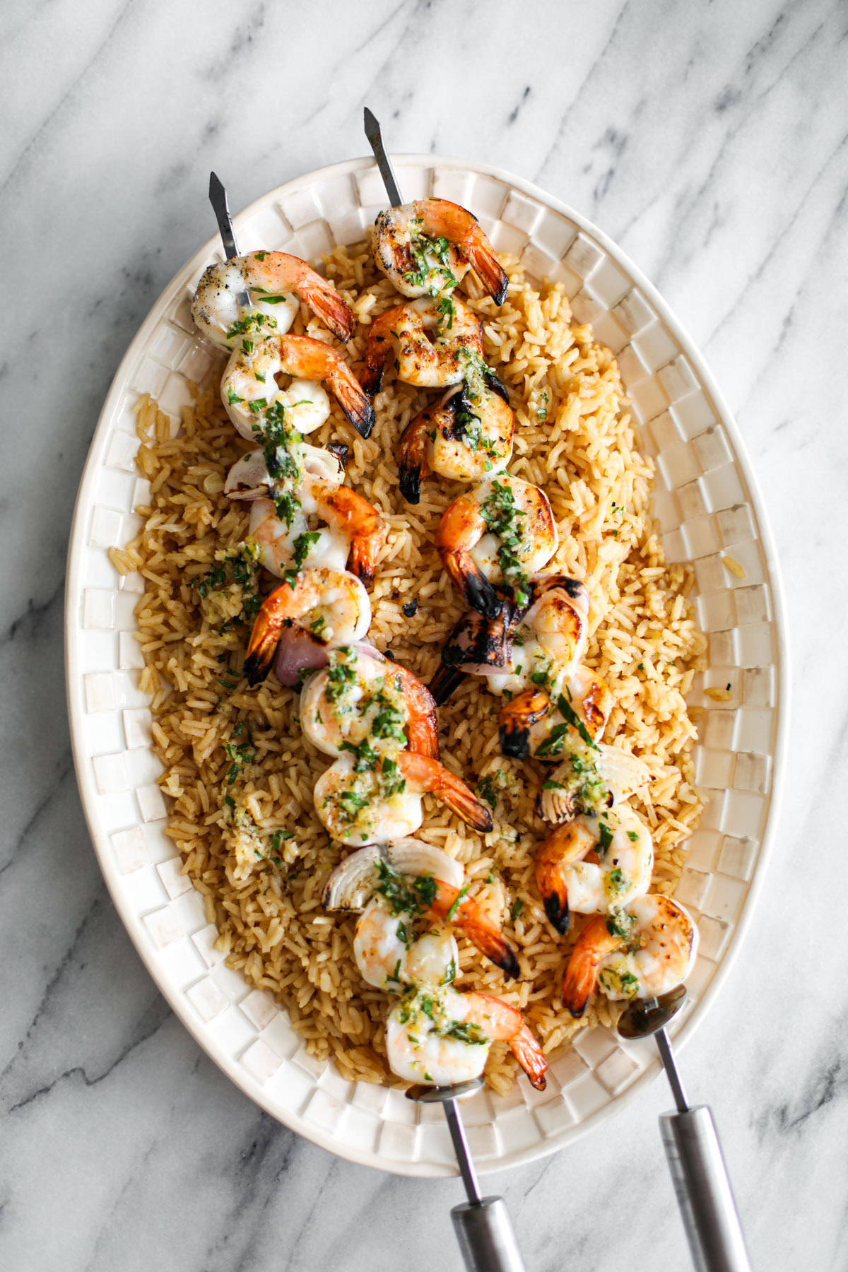 Two shrimp skewers atop a bed of rice on a white platter.