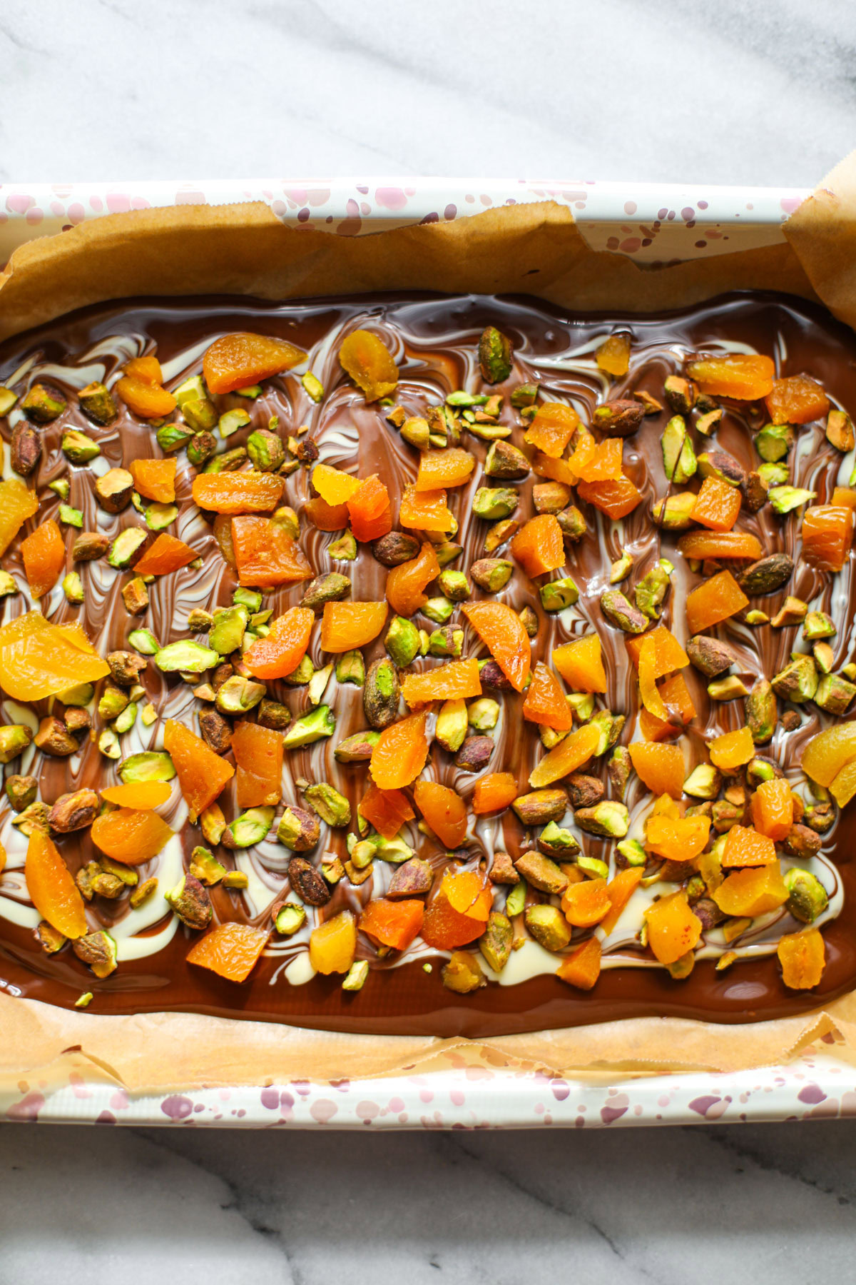 Marbled pistachio apricot chocolate bark on a pink speckled sheet tray.