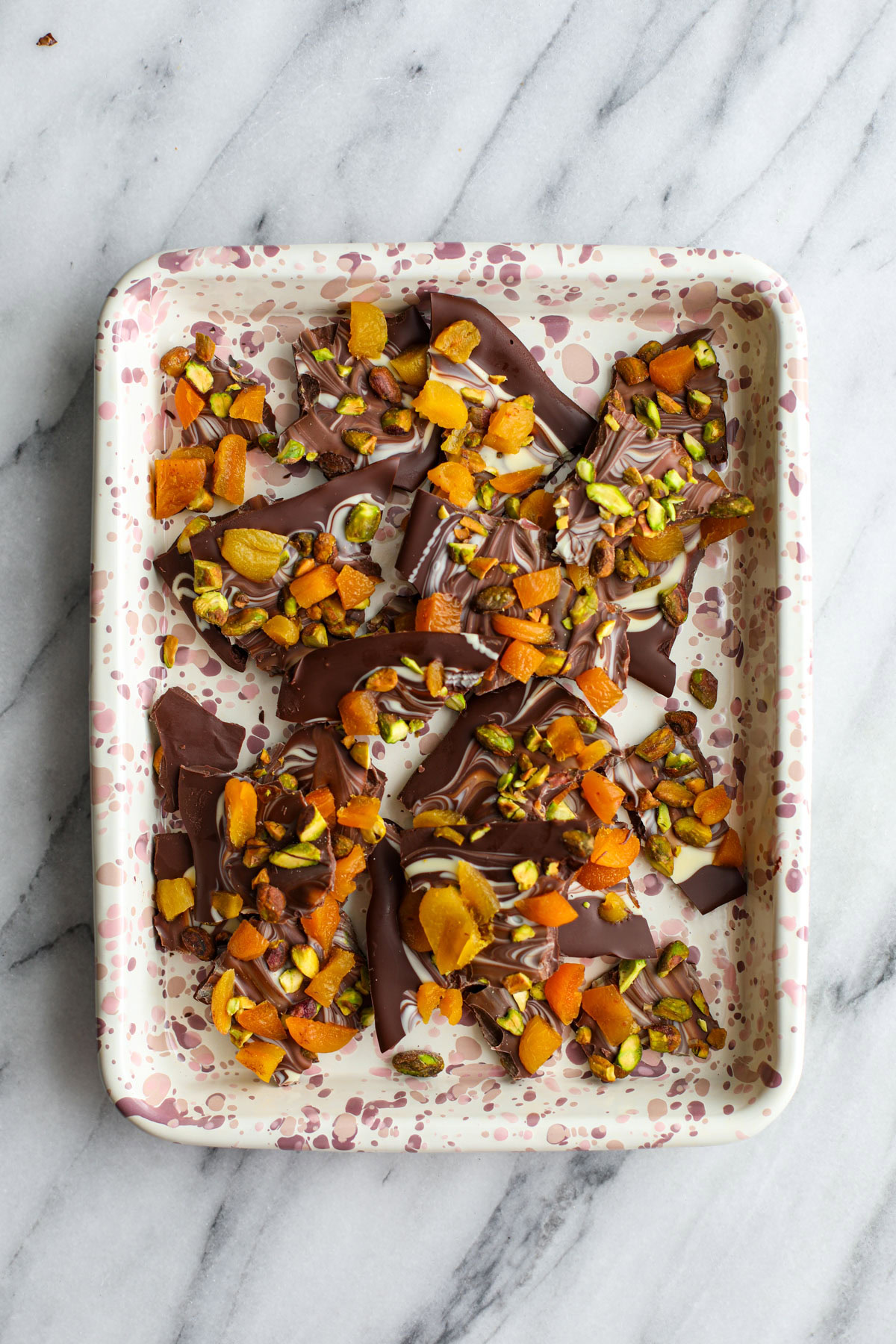 Marbled pistachio apricot chocolate bark on a pink speckled sheet tray.