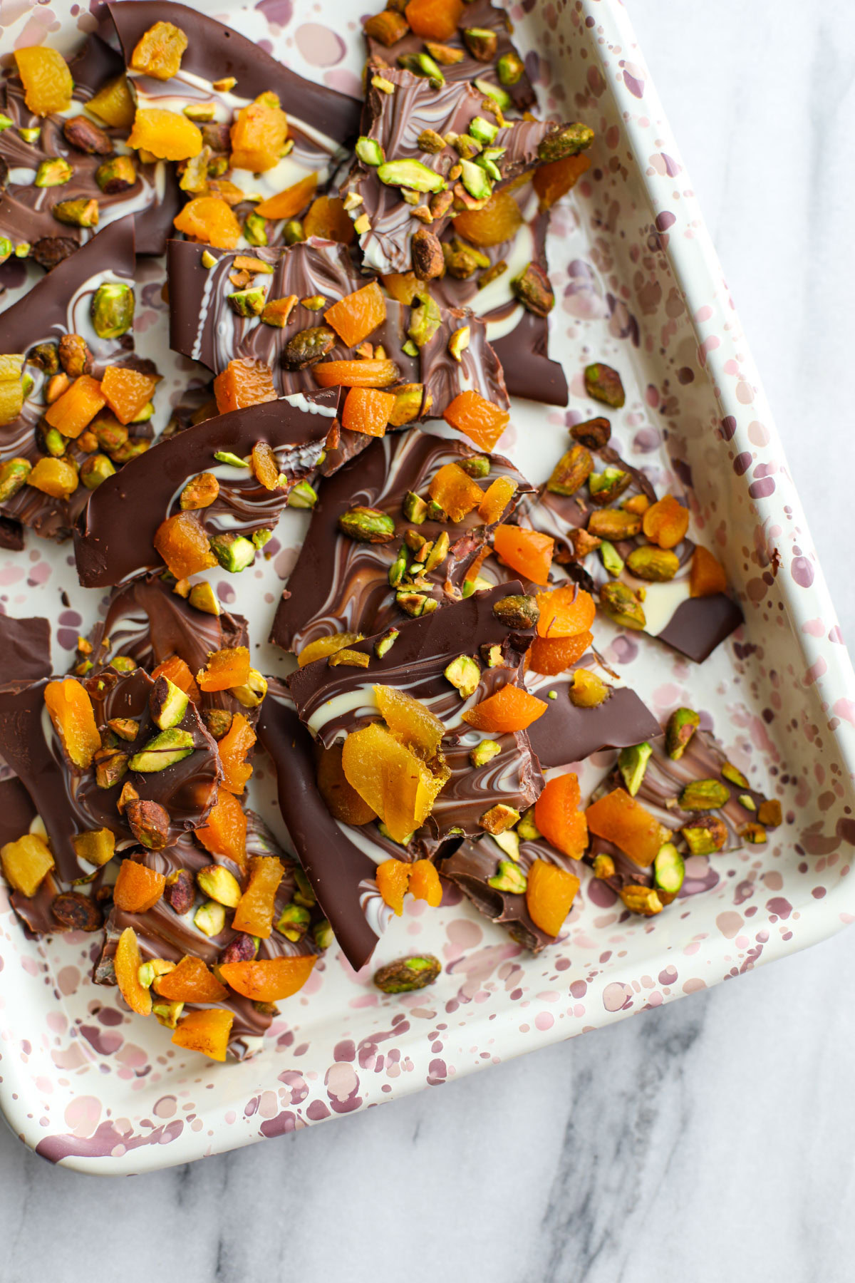 Marbled pistachio apricot chocolate bark on a pink speckled sheet tray.