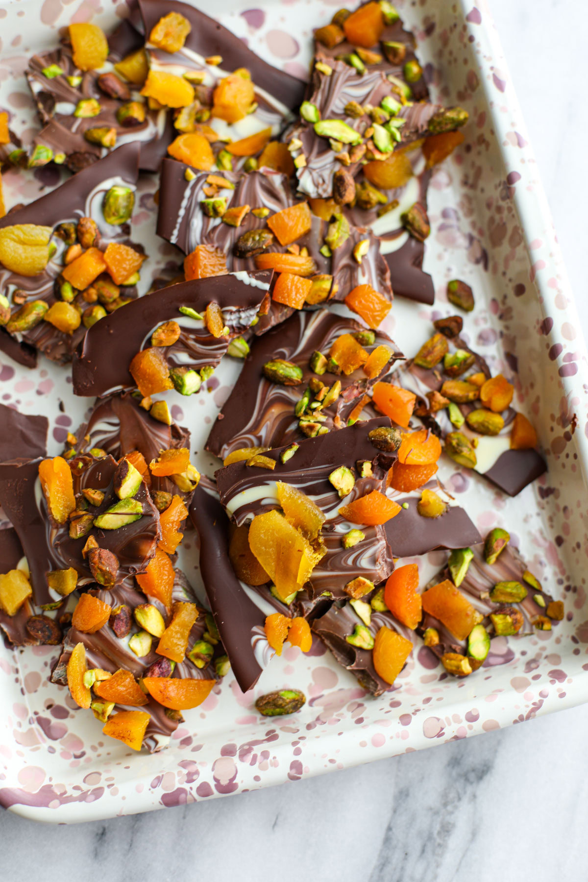 Marbled pistachio apricot chocolate bark on a pink speckled sheet tray.