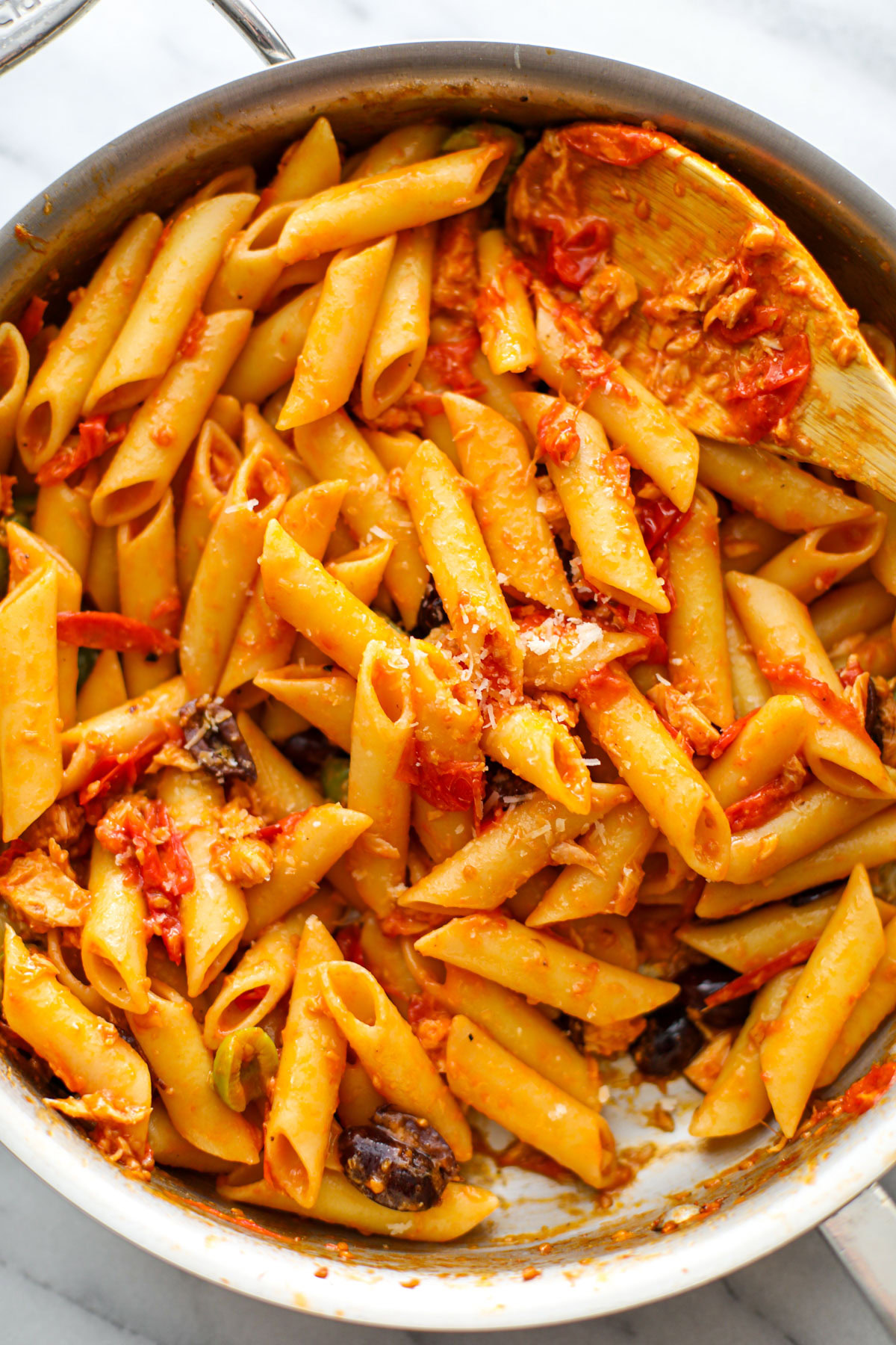 Up close of canned tuna pasta in a stainless skillet with a wooden spoon.