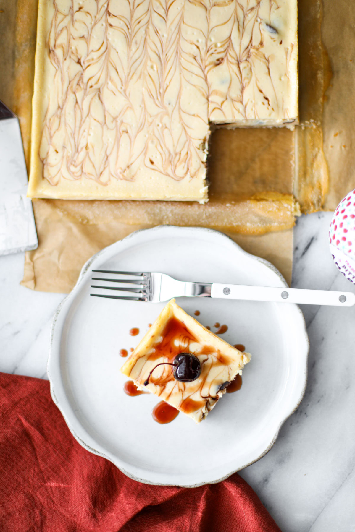 An amarena cherry cheesecake bar on a white plate with a white fork next to the 8x8 pan.