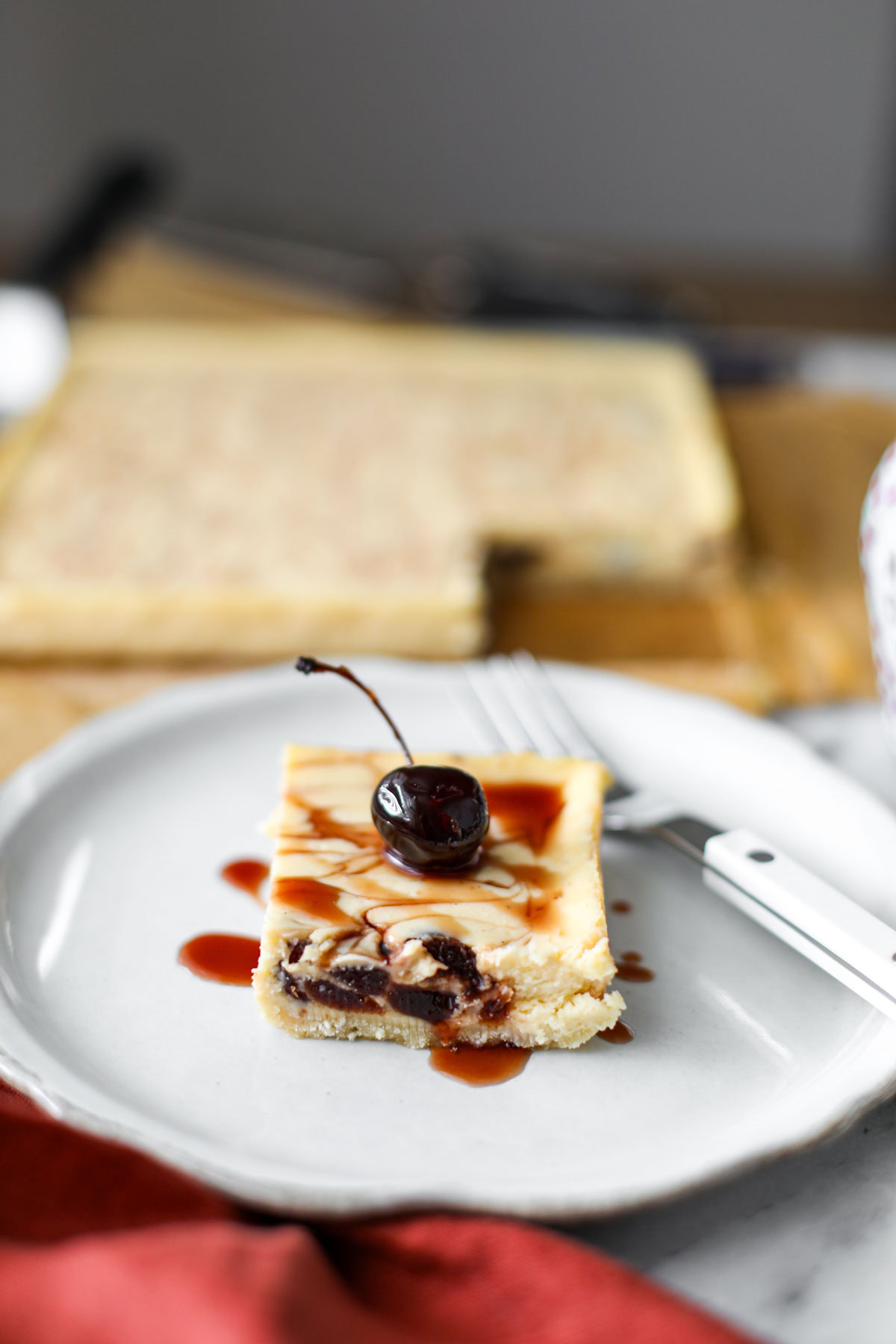 An amarena cherry cheesecake bar on a white plate with a white fork.