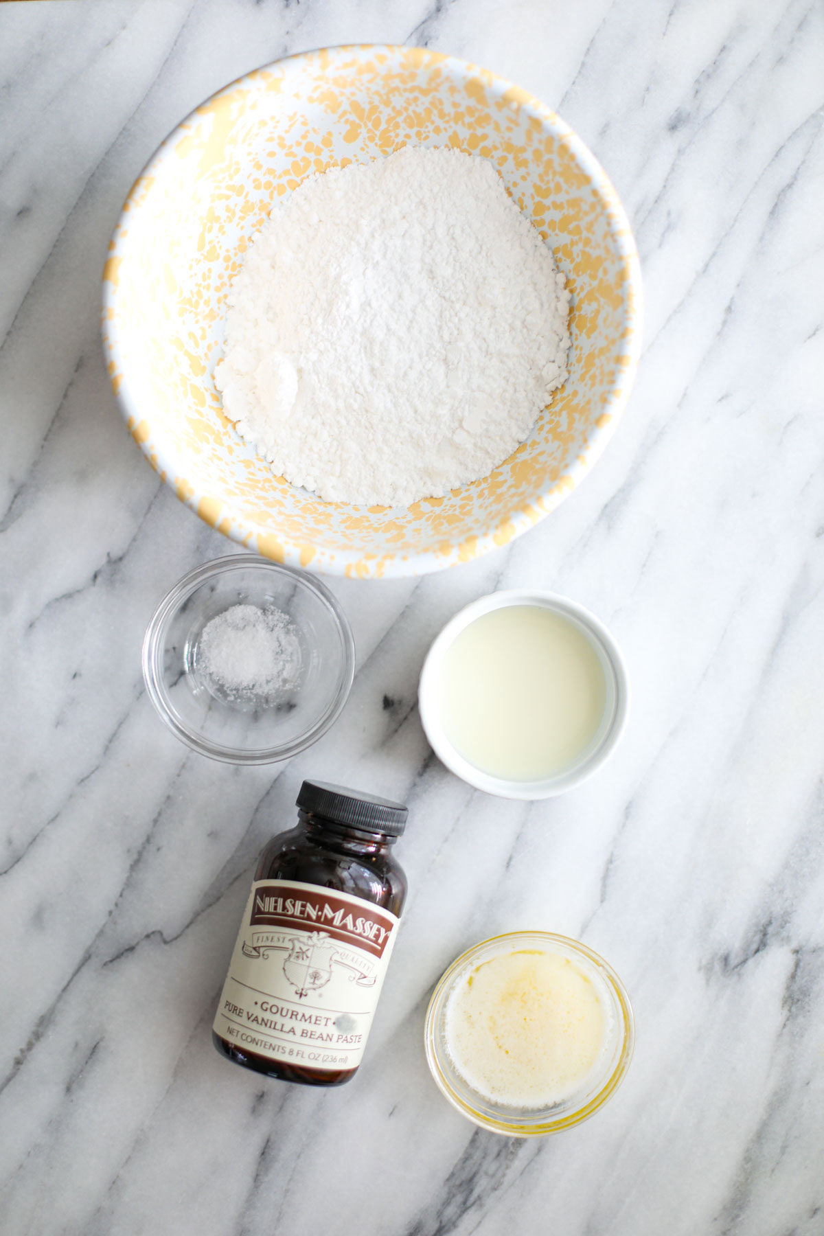 Ingredients to make vanilla bean glaze including powdered sugar, milk, salt, butter, and vanilla bean paste.