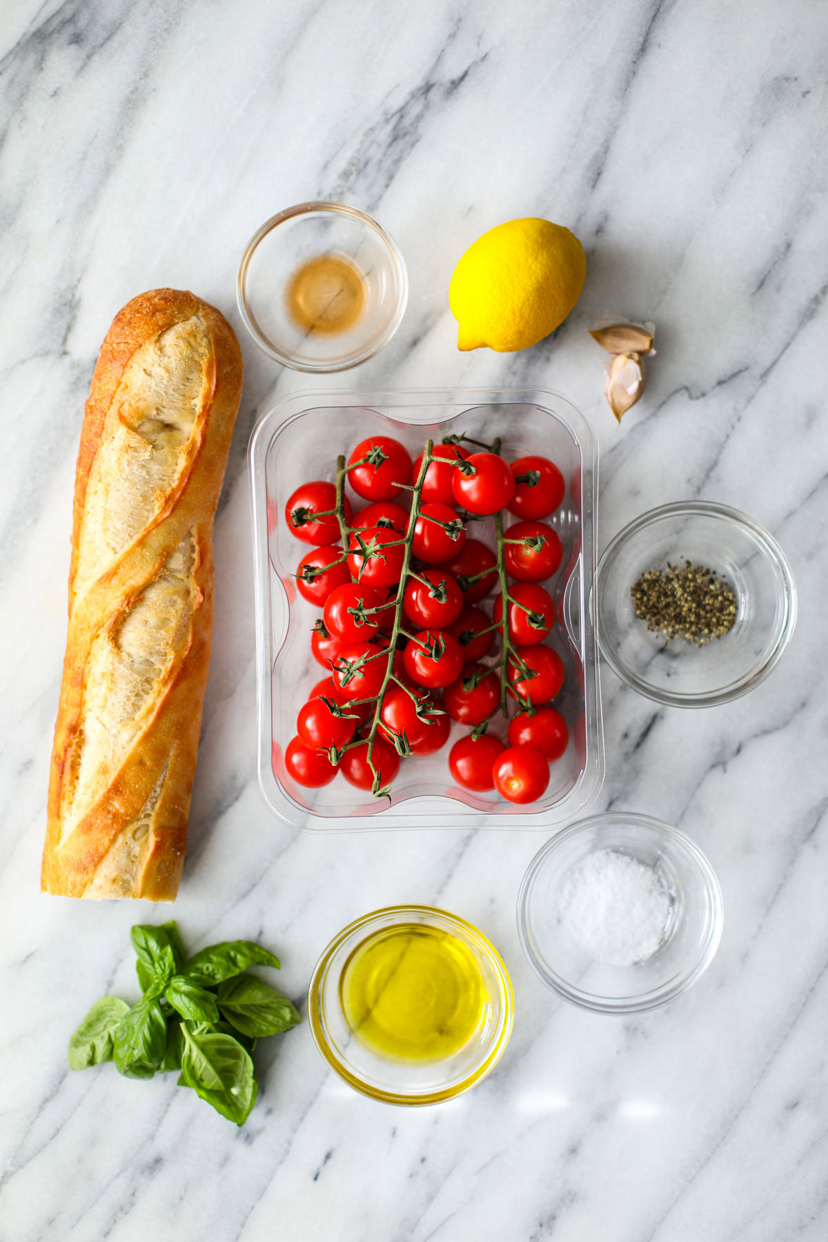 Ingredients to make bruschetta including cherry tomatoes, French bread, seasonings, oil, and basil.