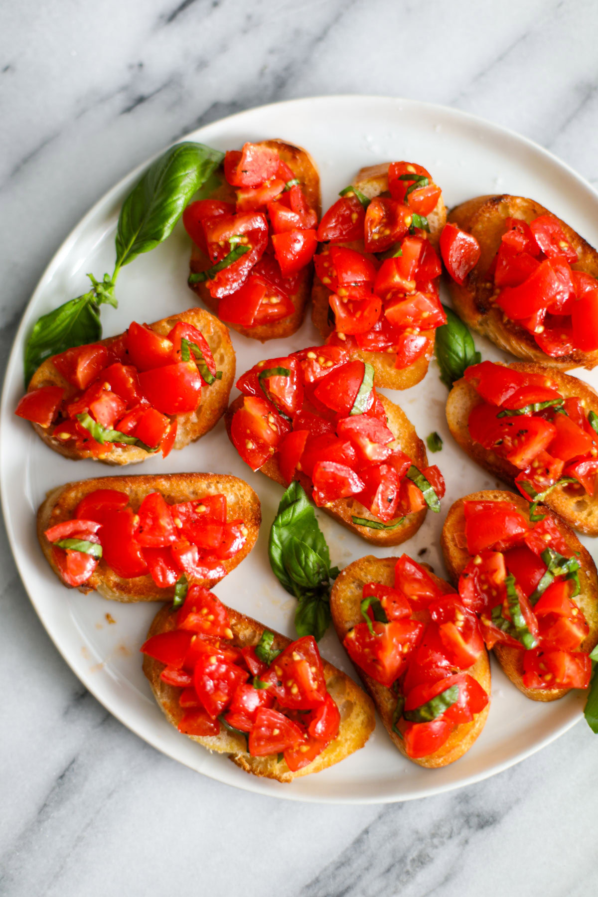 Cherry tomato bruschetta on a white plate garnished with basil.