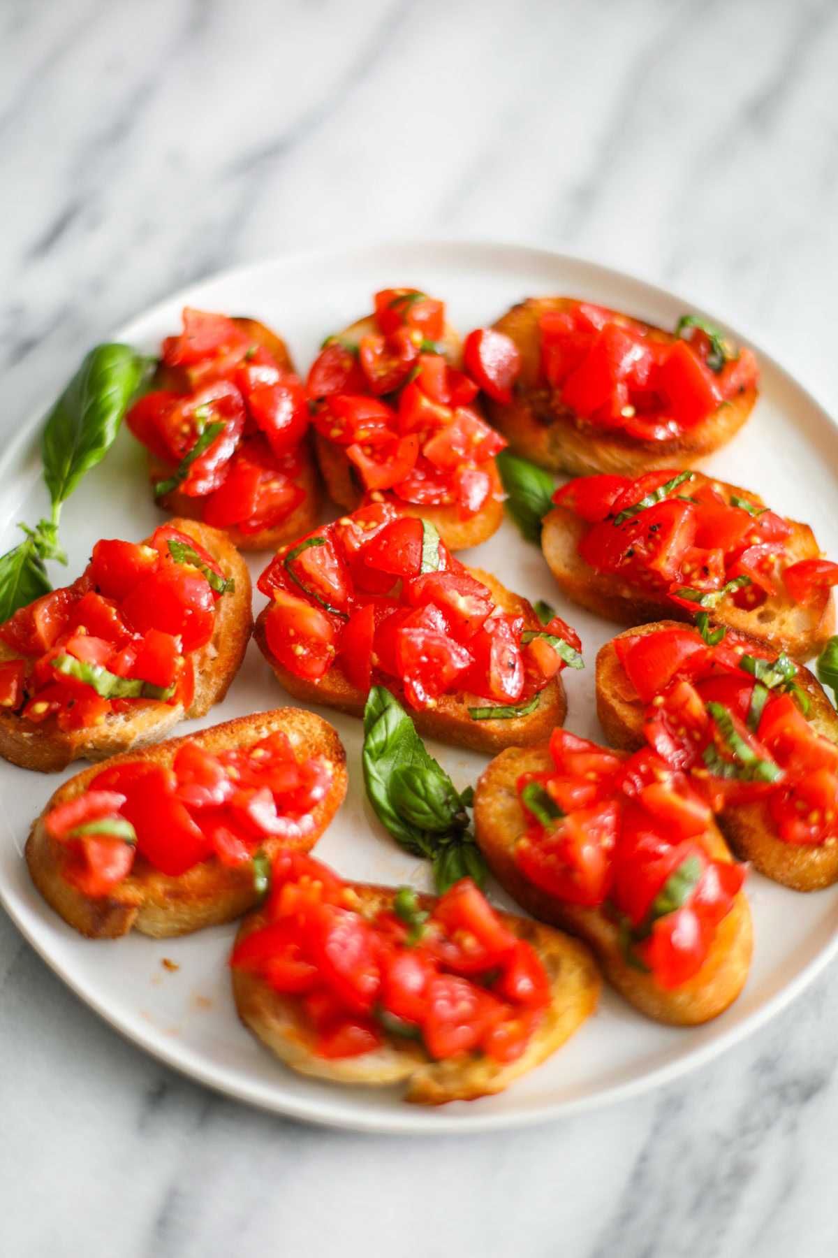 Cherry tomato bruschetta on a white plate garnished with basil.