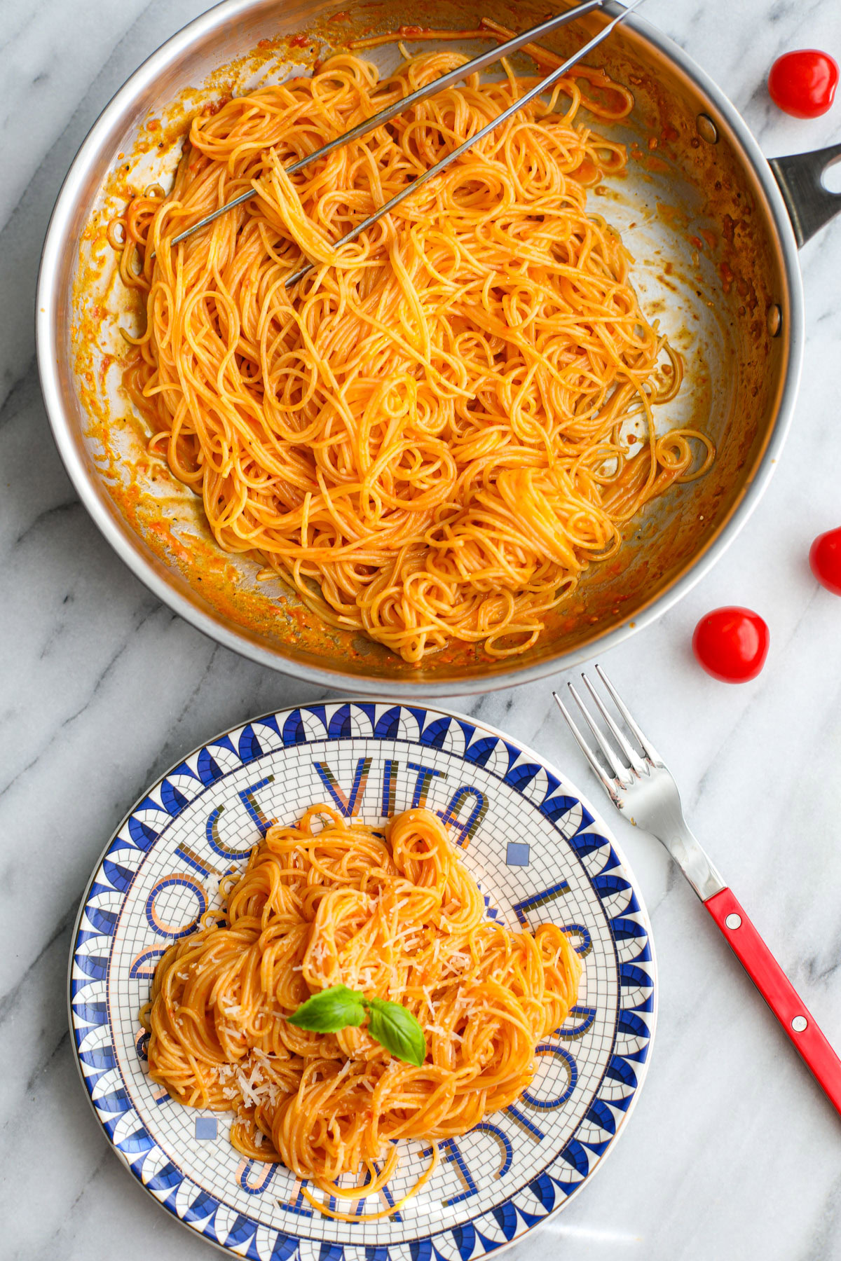 Cherry tomato pasta sauce coated spaghetti on a blue and white plate with a skillet of pasta behind it.