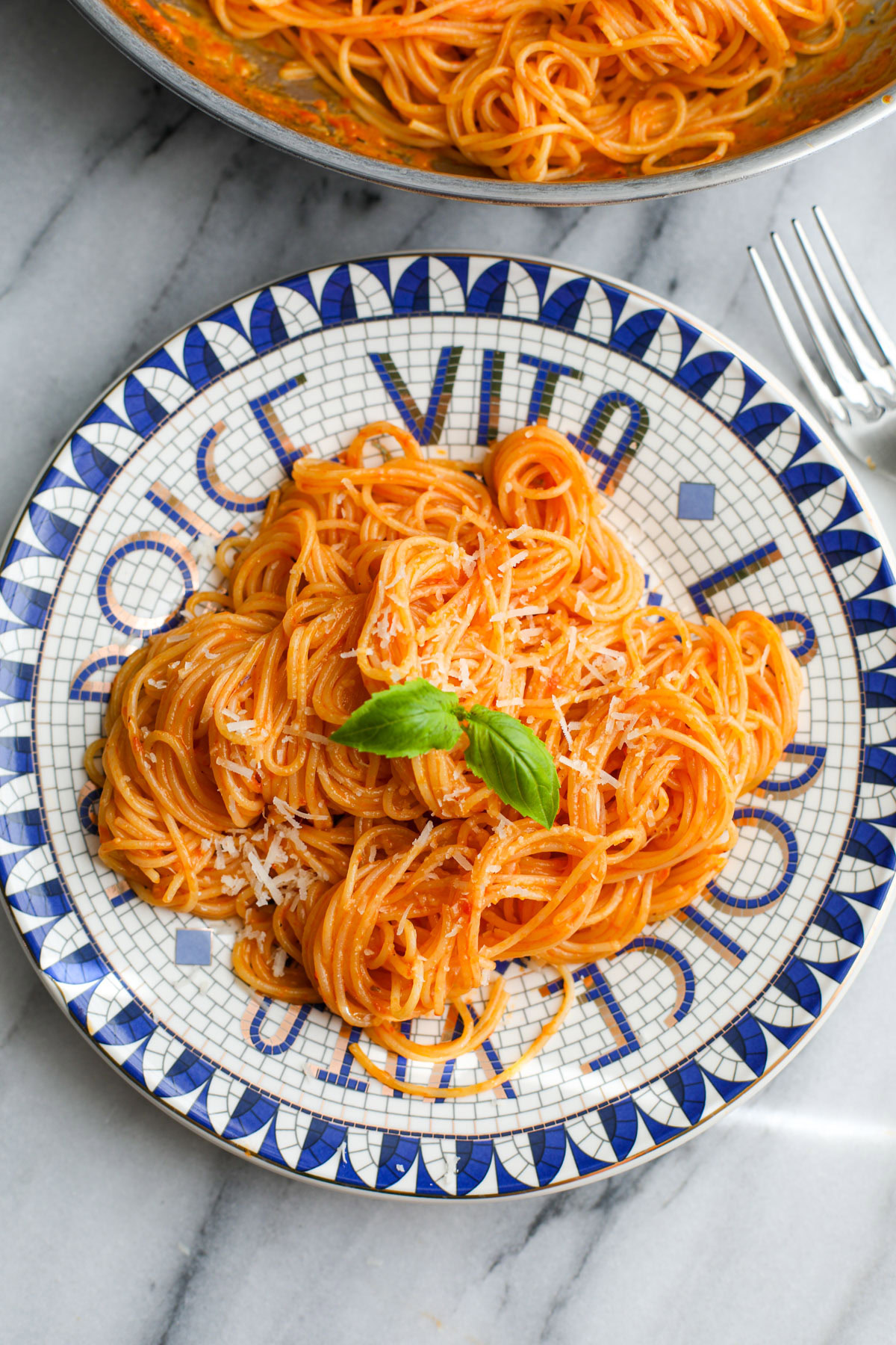 Cherry tomato pasta sauce coated spaghetti on a blue and white plate topped with a sprig of basil.
