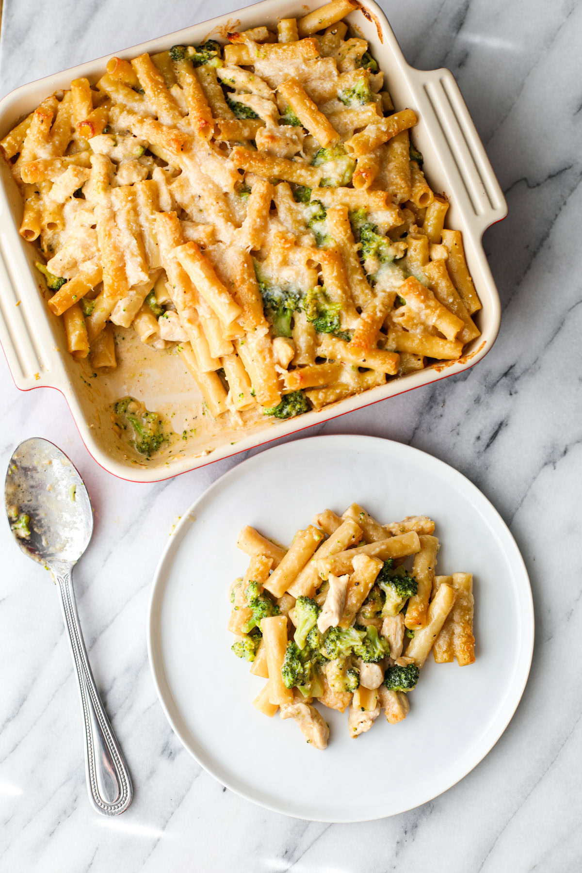 A white plate with chicken broccoli ziti. 