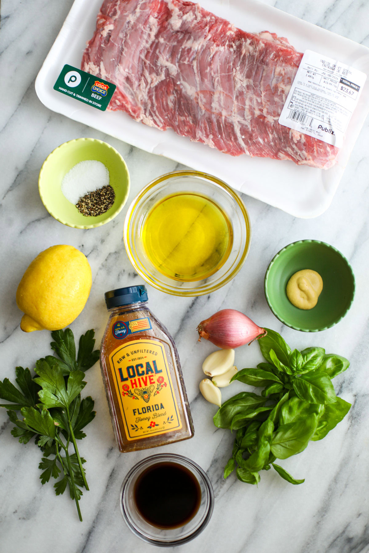 ingredients for skirt steak marinade including skirt, steak, seasonings, oil, mustard, shallot, garlic, basil, parsley, honey, and a lemon.