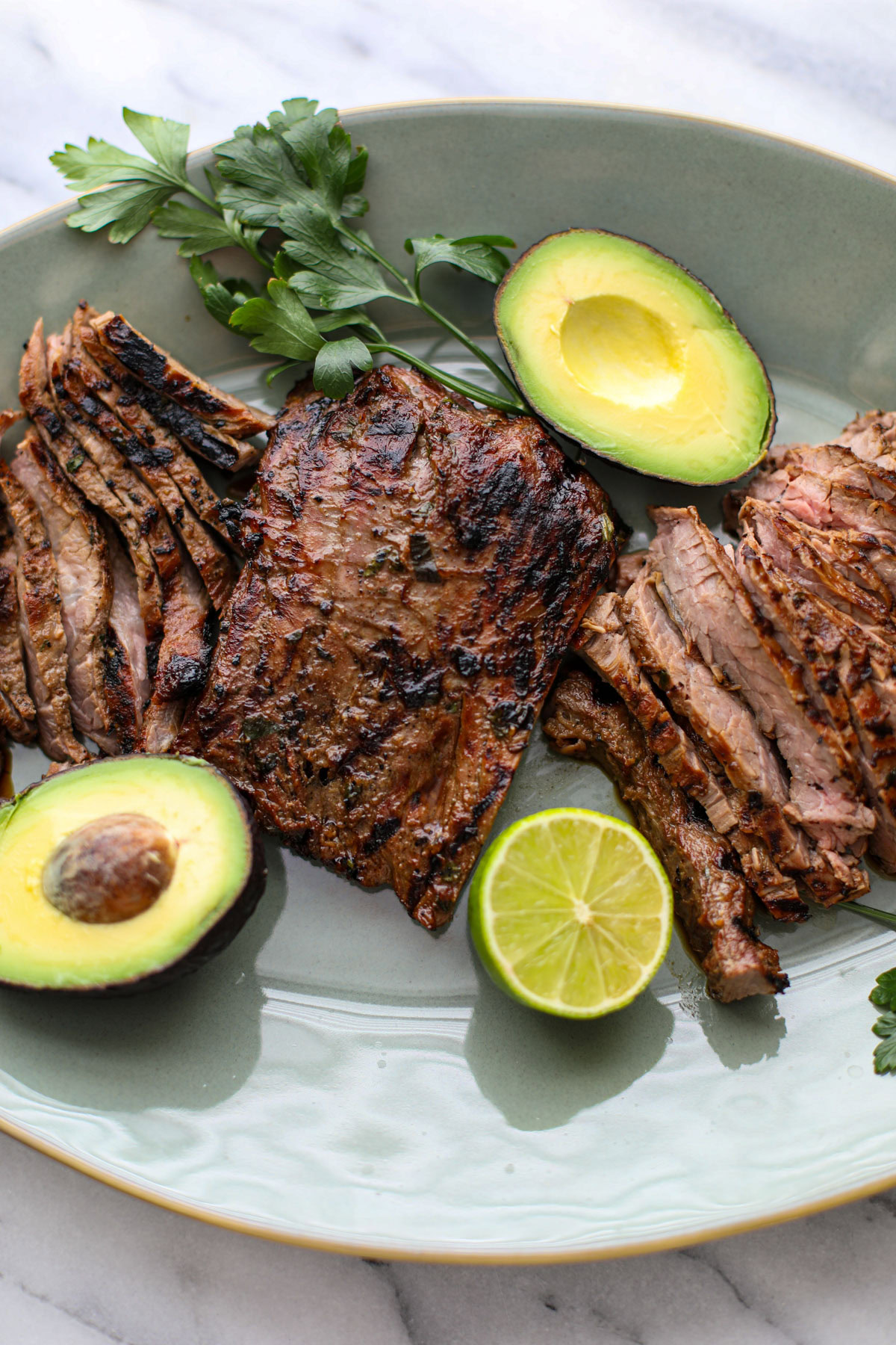A green platter of sliced skirt steak with a skirt steak marinade.