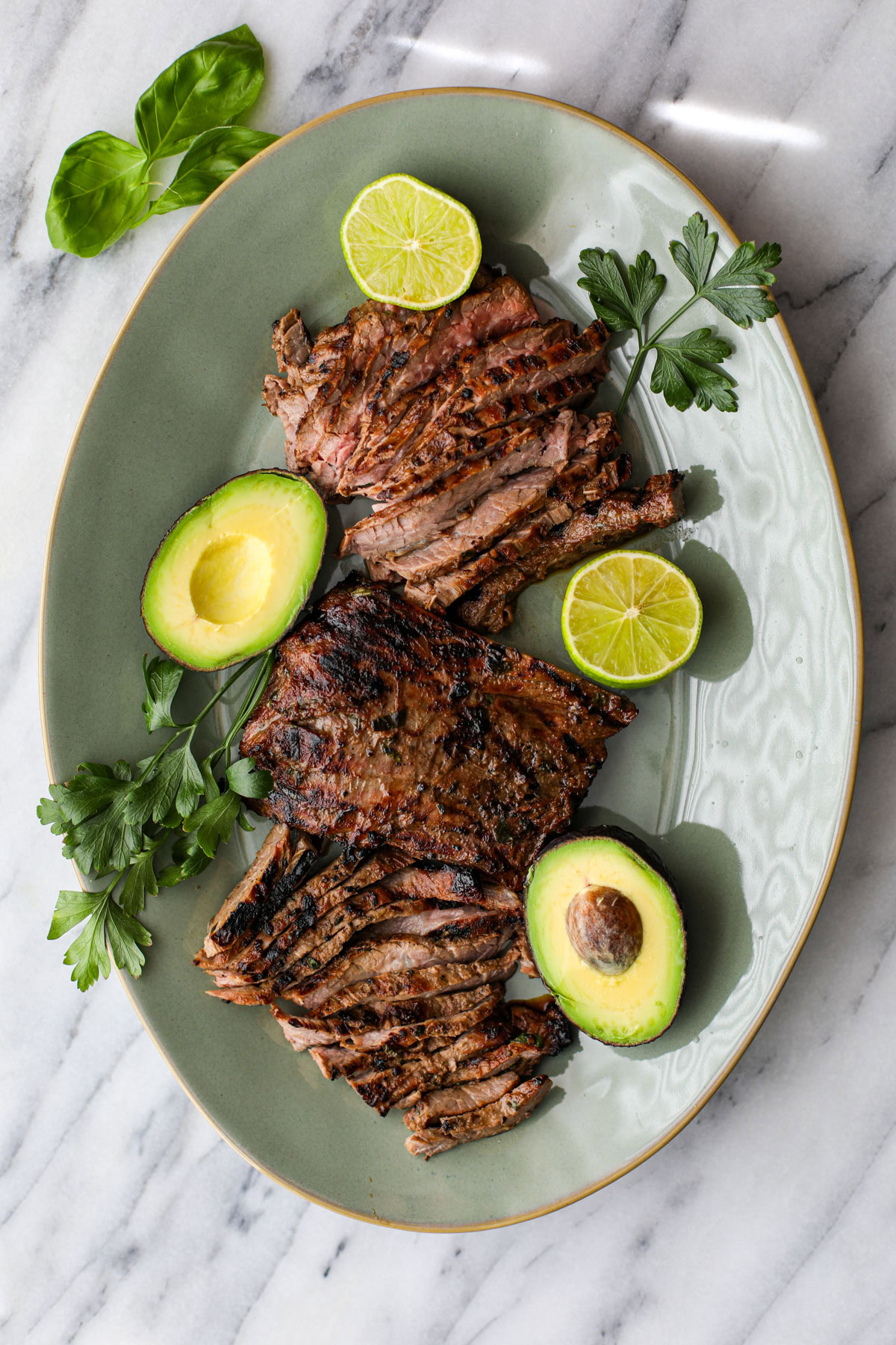 A green platter of sliced skirt steak with a skirt steak marinade.