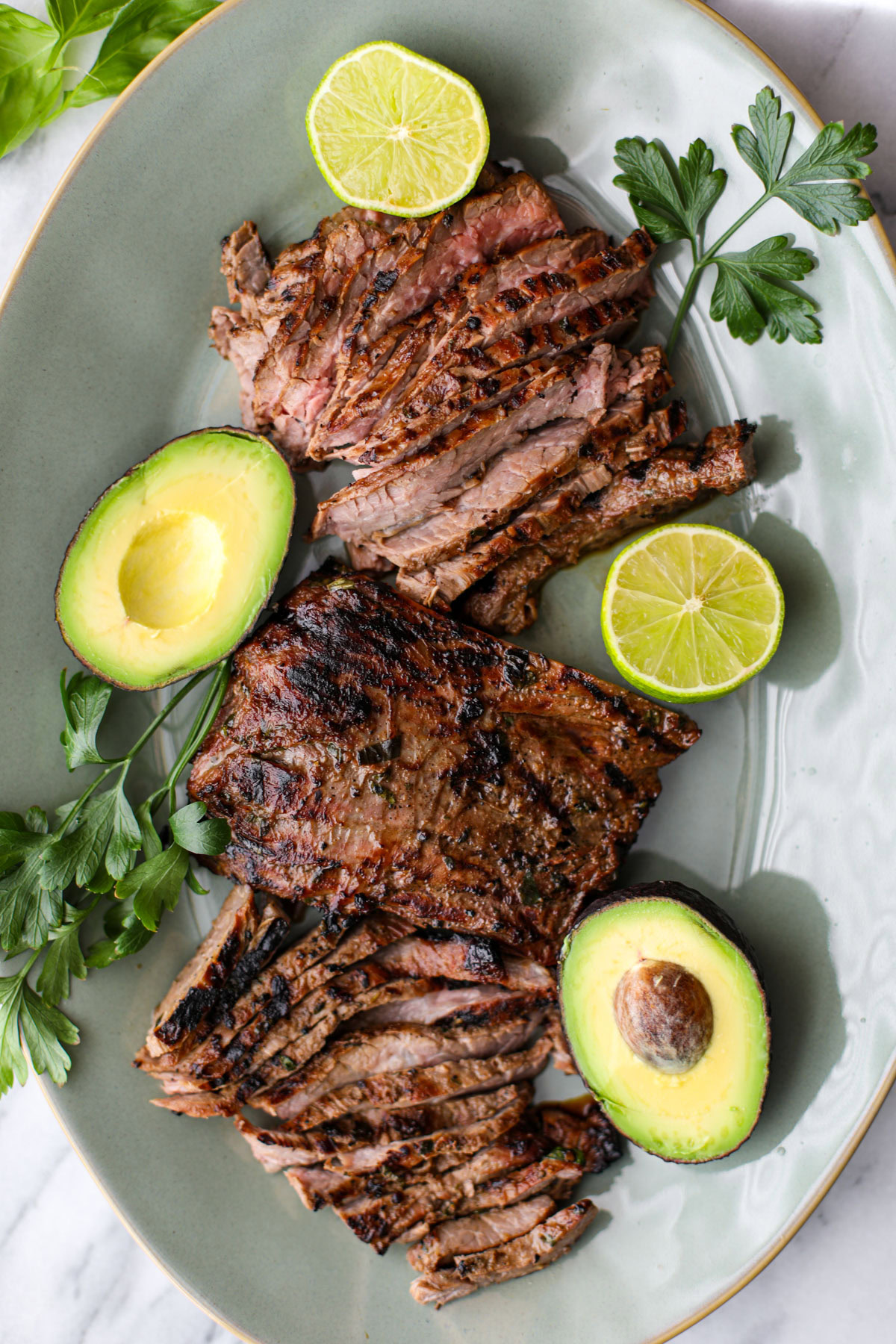 A green platter of sliced skirt steak with a skirt steak marinade.