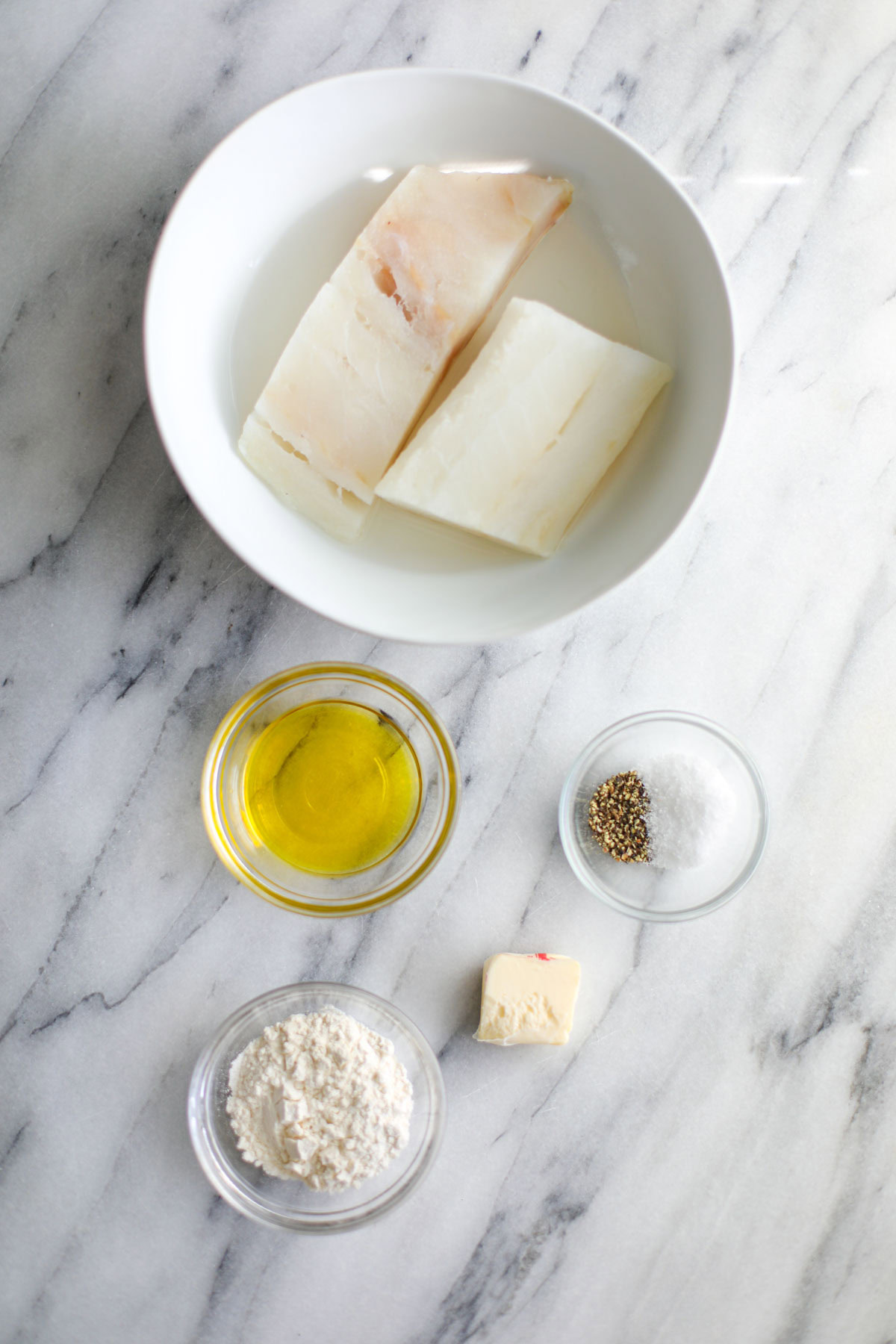 A bowl of cod, olive oil, seasonings, flour, and butter.