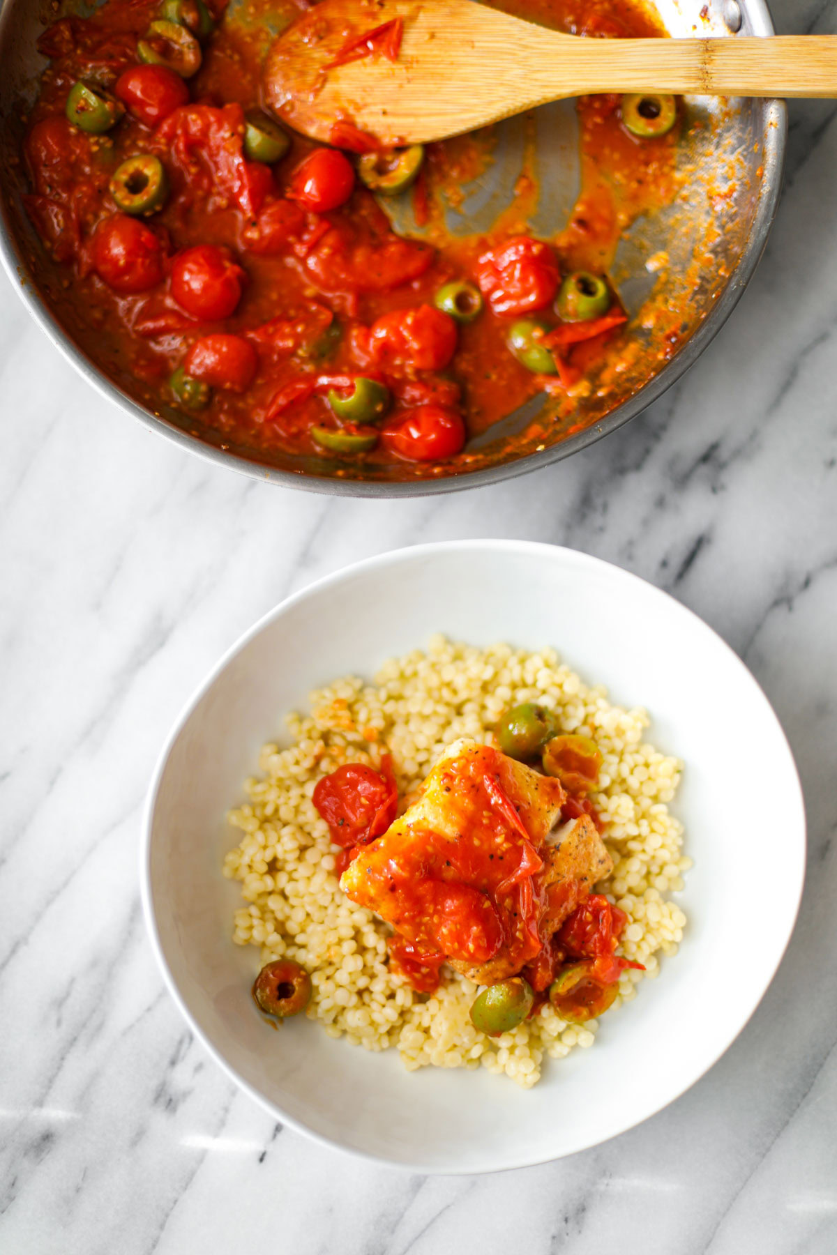A white bowl of couscous with pan seared cod and jammy cherry tomatoes.