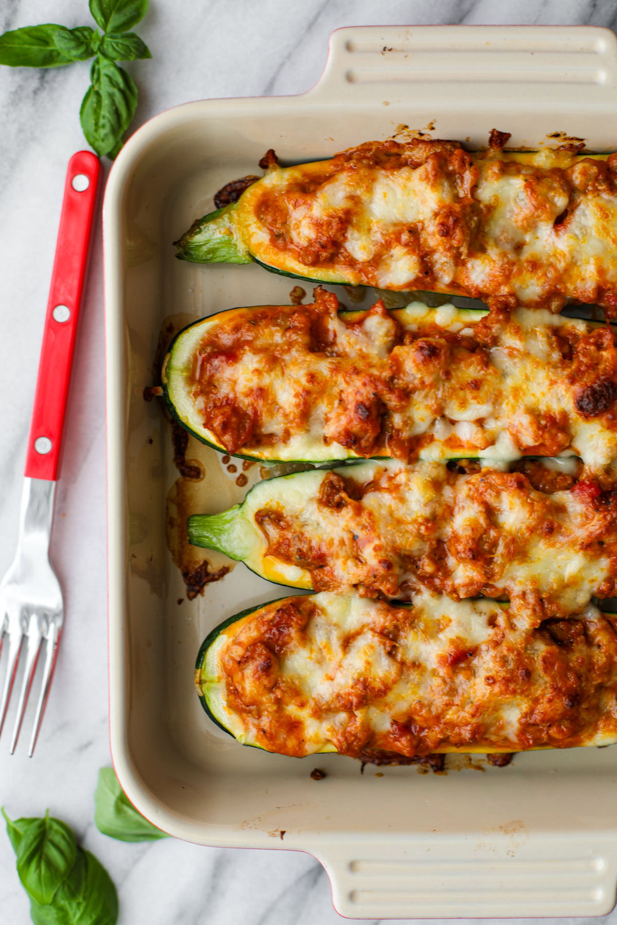 Sausage stuffed zucchini boats in a square baking dish with a red fork.