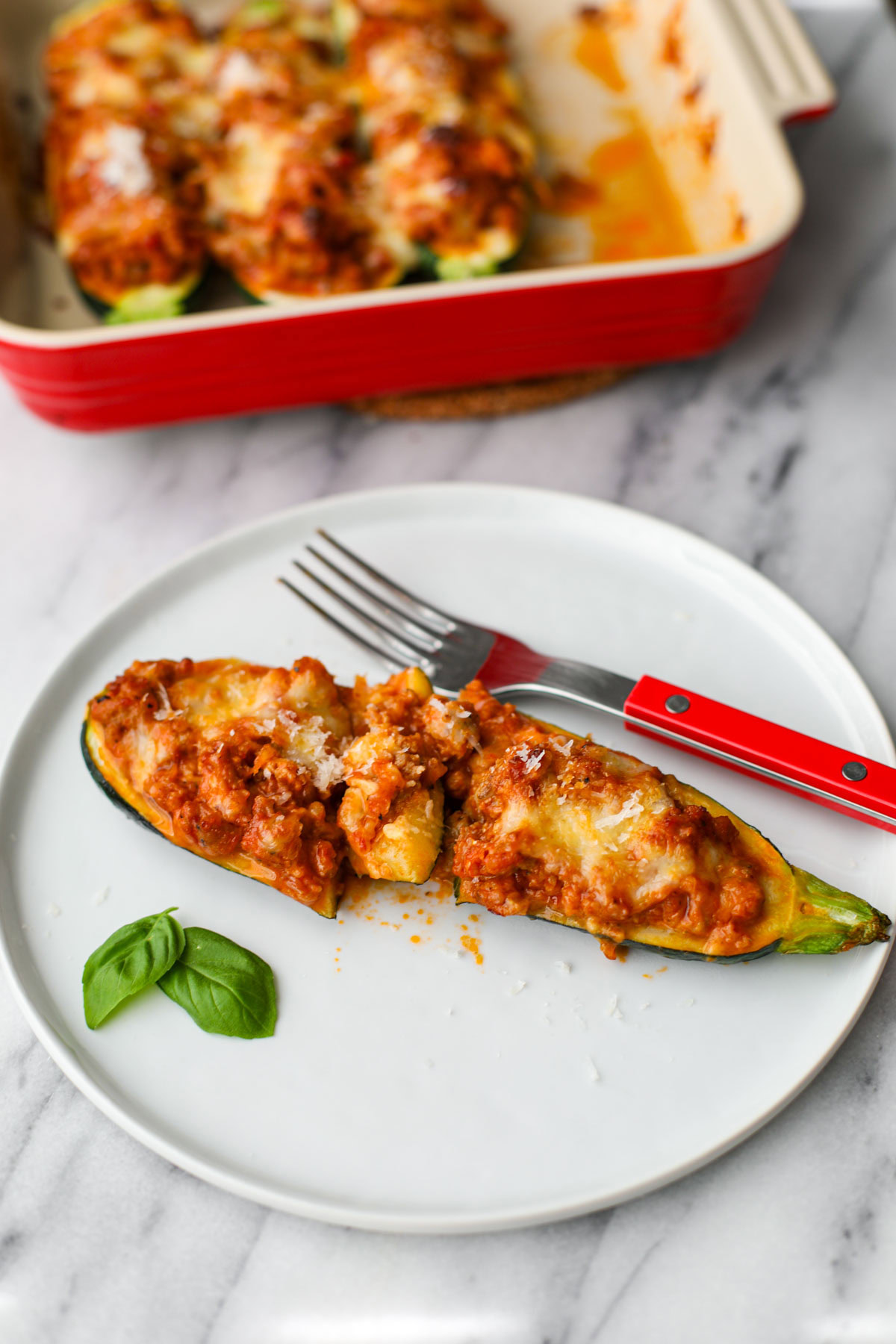 A zucchini boat on a white plate with a red fork.