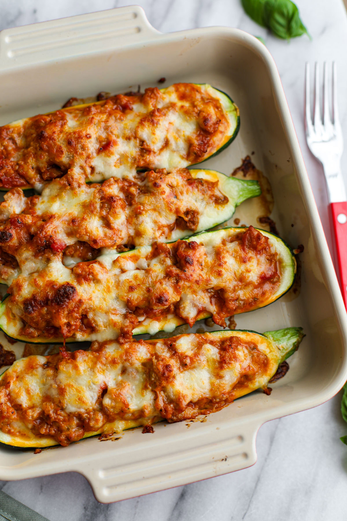 Sausage stuffed zucchini boats in a square baking dish with a red fork.