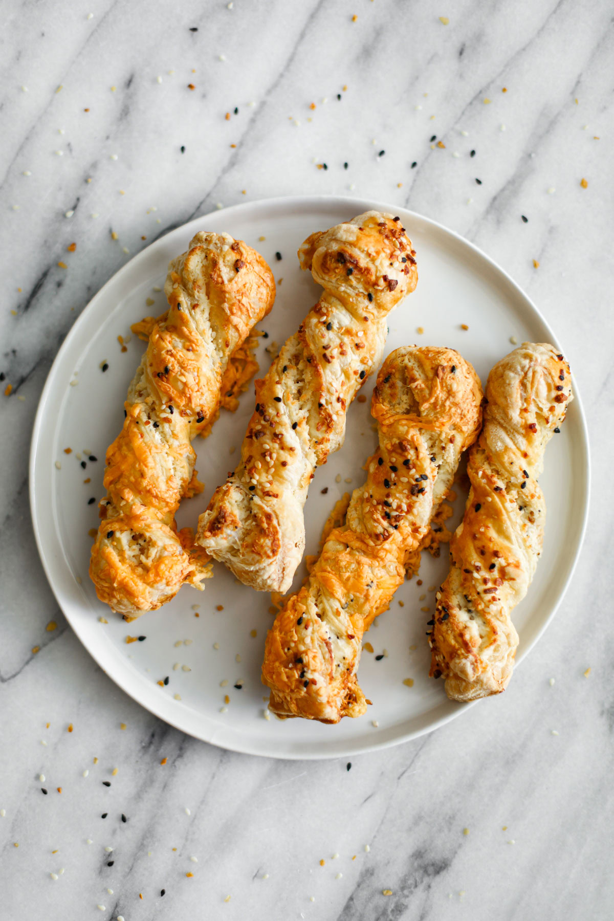 Everything bagel puff pastry twists on a white plate. 