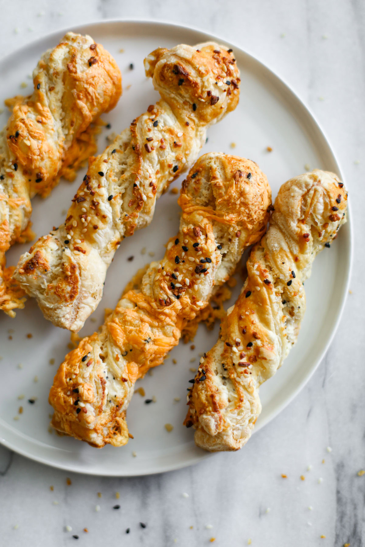 Everything bagel puff pastry twists on a white plate. 