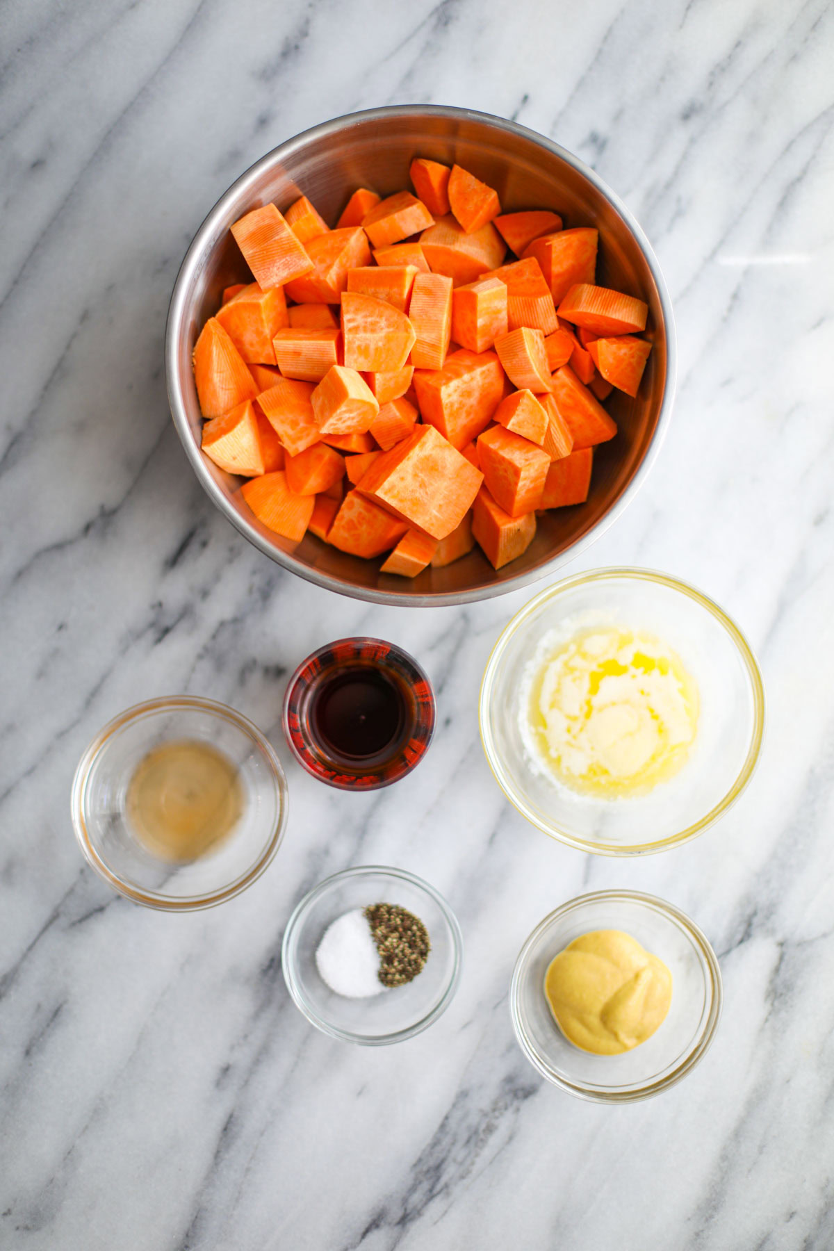 A bowl of sweet potatoes, melted butter, maple syrup, vinegar, seasonings, and dijon mustard.