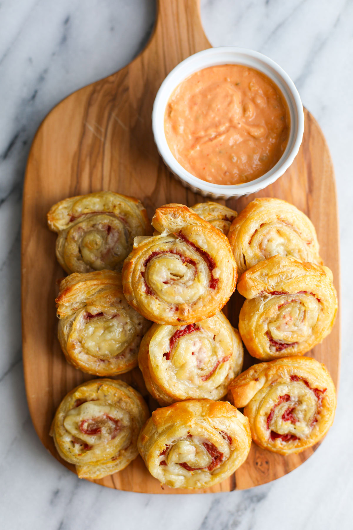 Reuben pinwheels on an oblong wood cutting board with thousand island dressing in a white bowl.