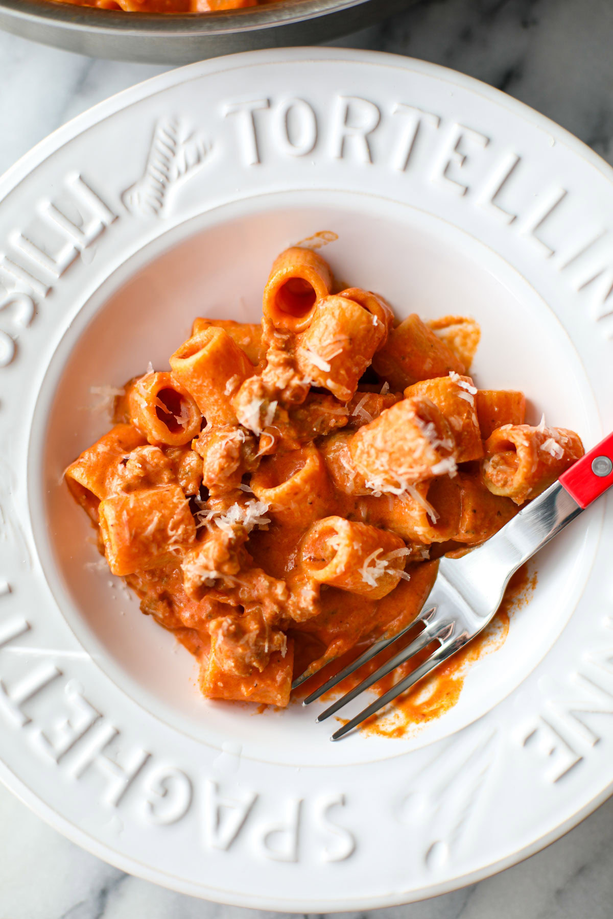 A white bowl of creamy sausage rigatoni.