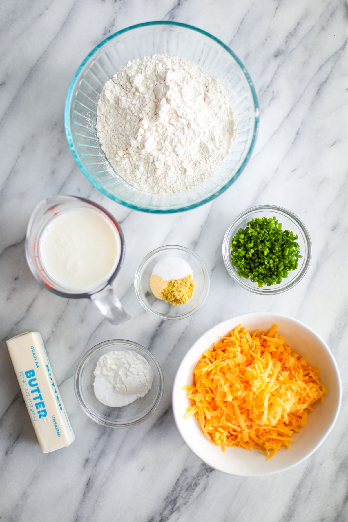 Ingredients for cheddar chive biscuits including cheddar, Parmesan, chives, butter, and buttermilk