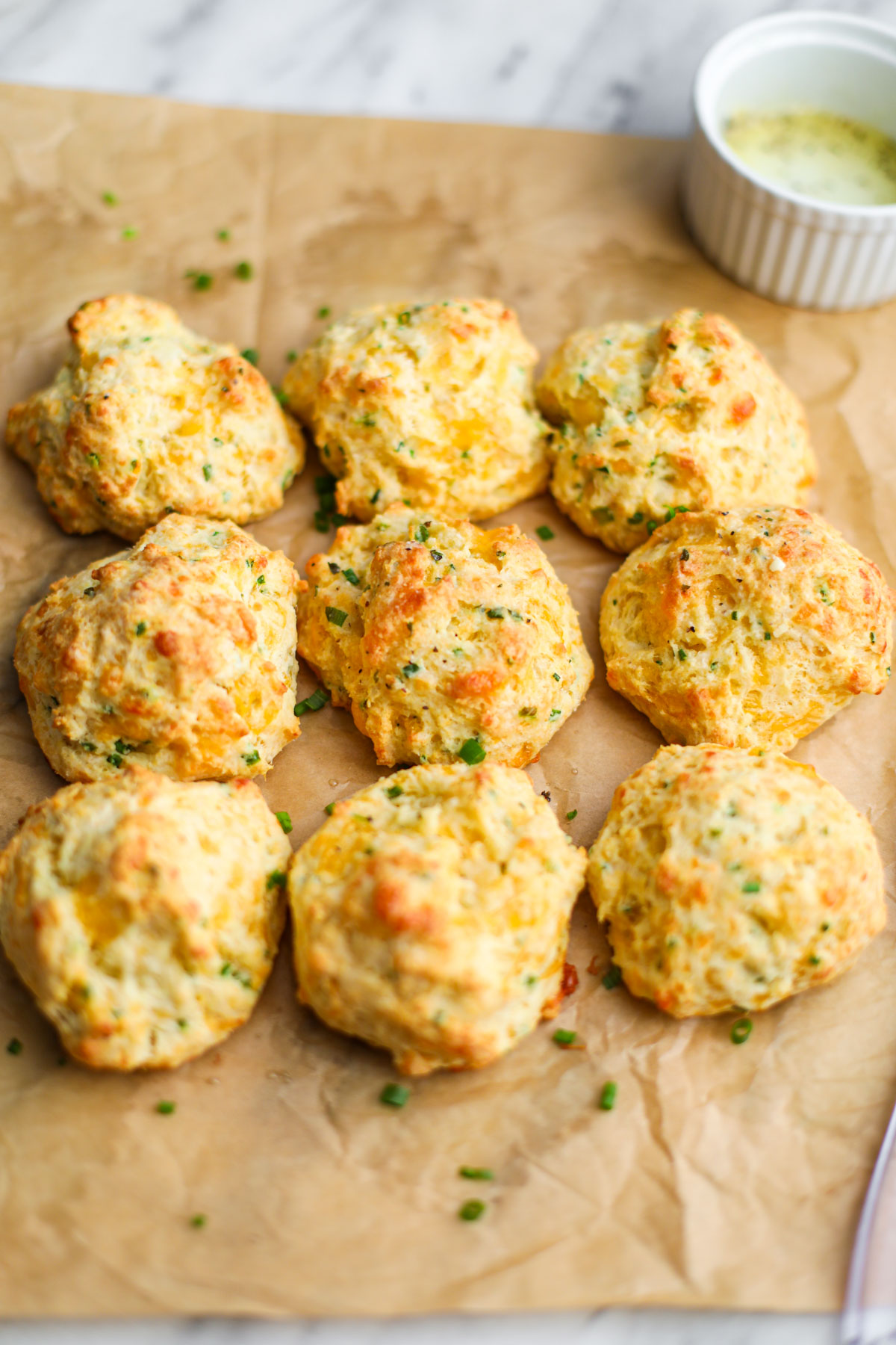 Cheddar chive biscuits brushed with garlic butter on a parchment-lined baking sheet