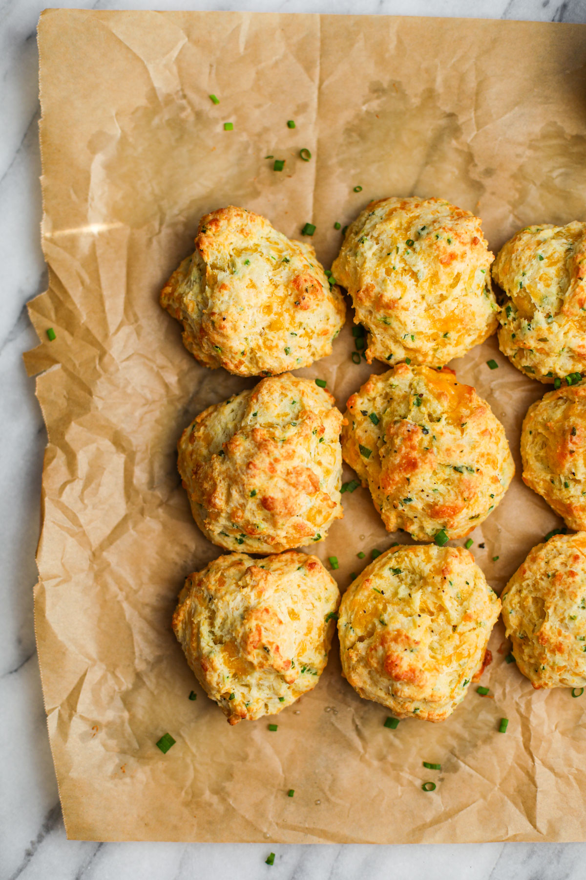 Cheddar chive biscuits on a parchment-lined baking sheet.