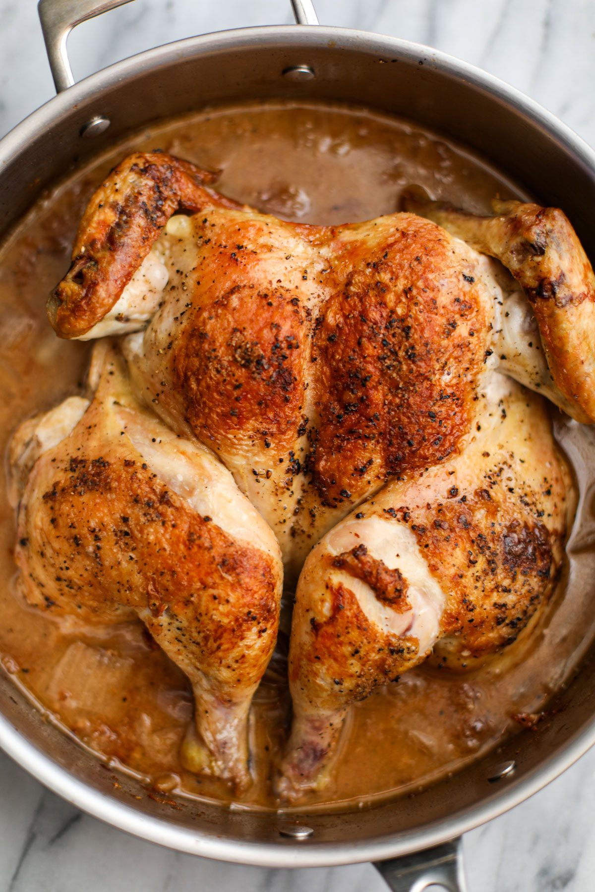 A roasted spatchcock chicken in a stainless steel skillet. 