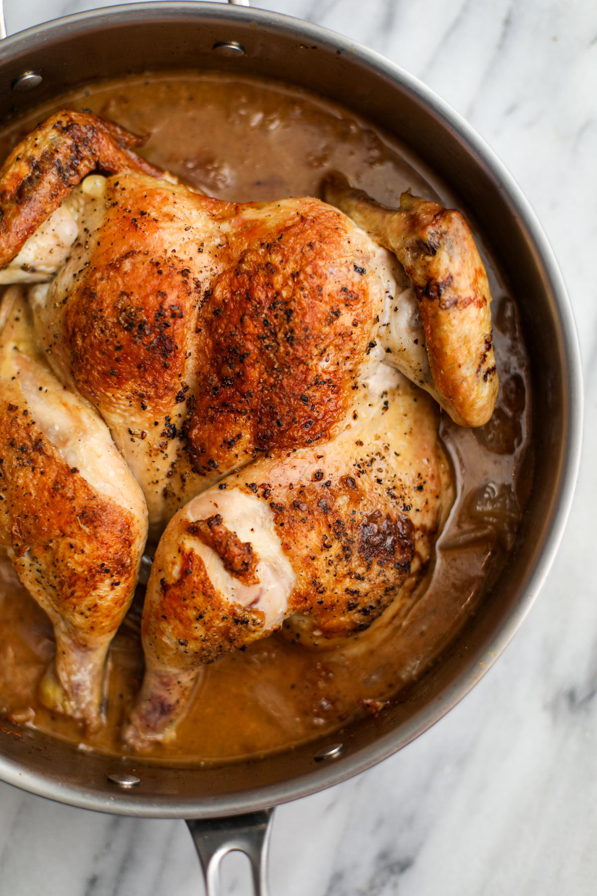 A roasted spatchcock chicken in a stainless steel skillet. 