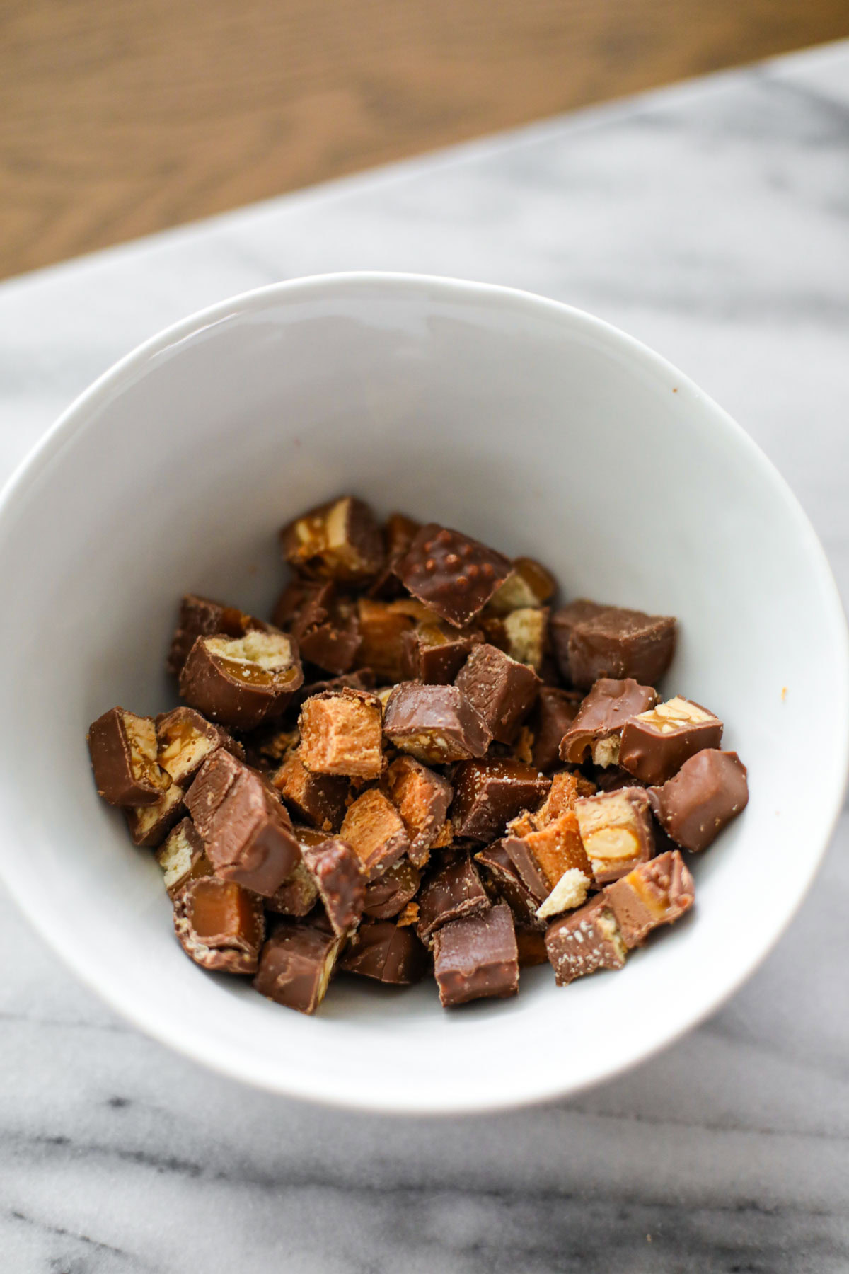 White bowl of chopped leftover Halloween candy for cookie bars.