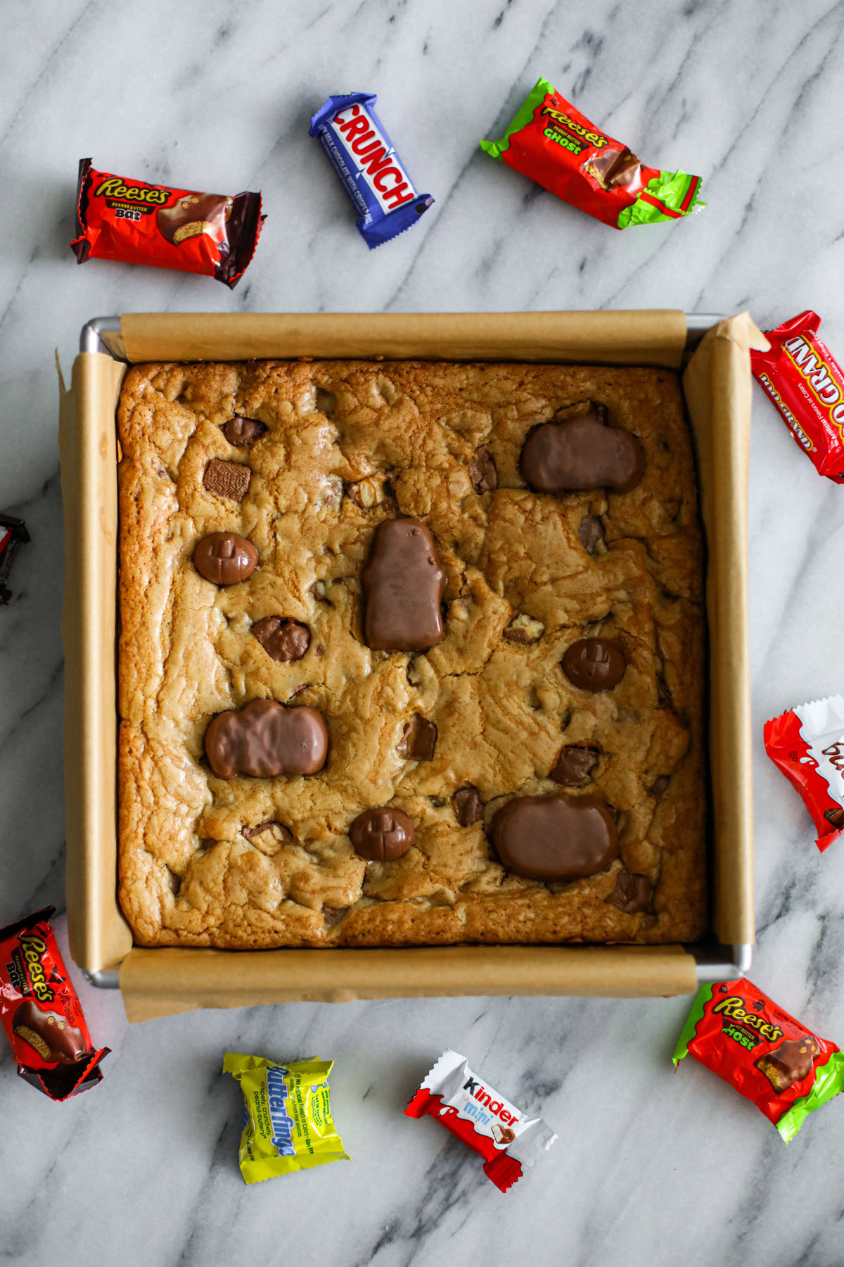 Leftover Halloween candy cookie bars sliced into squares, topped with chopped chocolate candy and flaky salt.