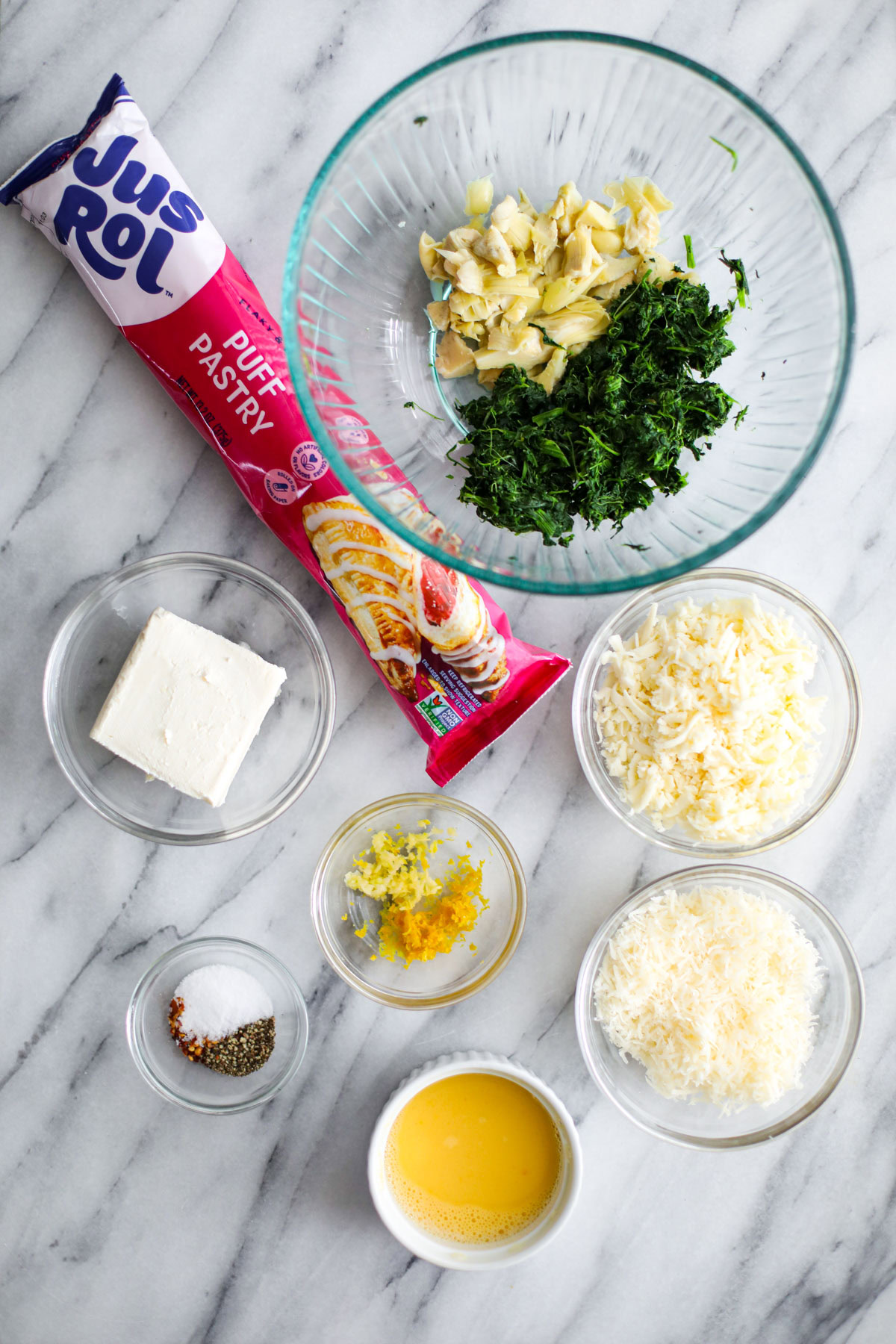 Ingredients for spinach and artichoke pinwheels, including puff pastry, cream cheese, spinach, artichoke hearts, and cheeses.
