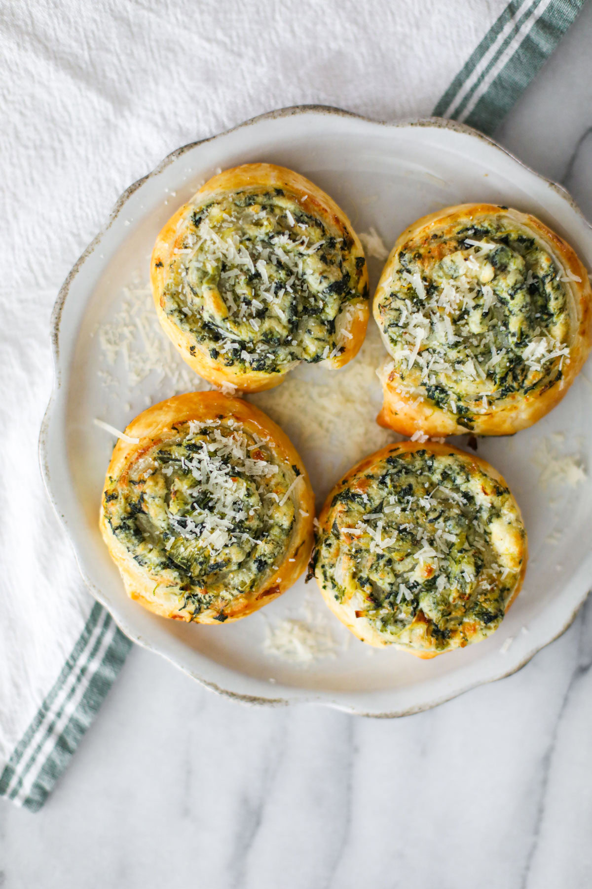 Golden spinach and artichoke pinwheels on a serving platter, sprinkled with grated Parmigiano Reggiano